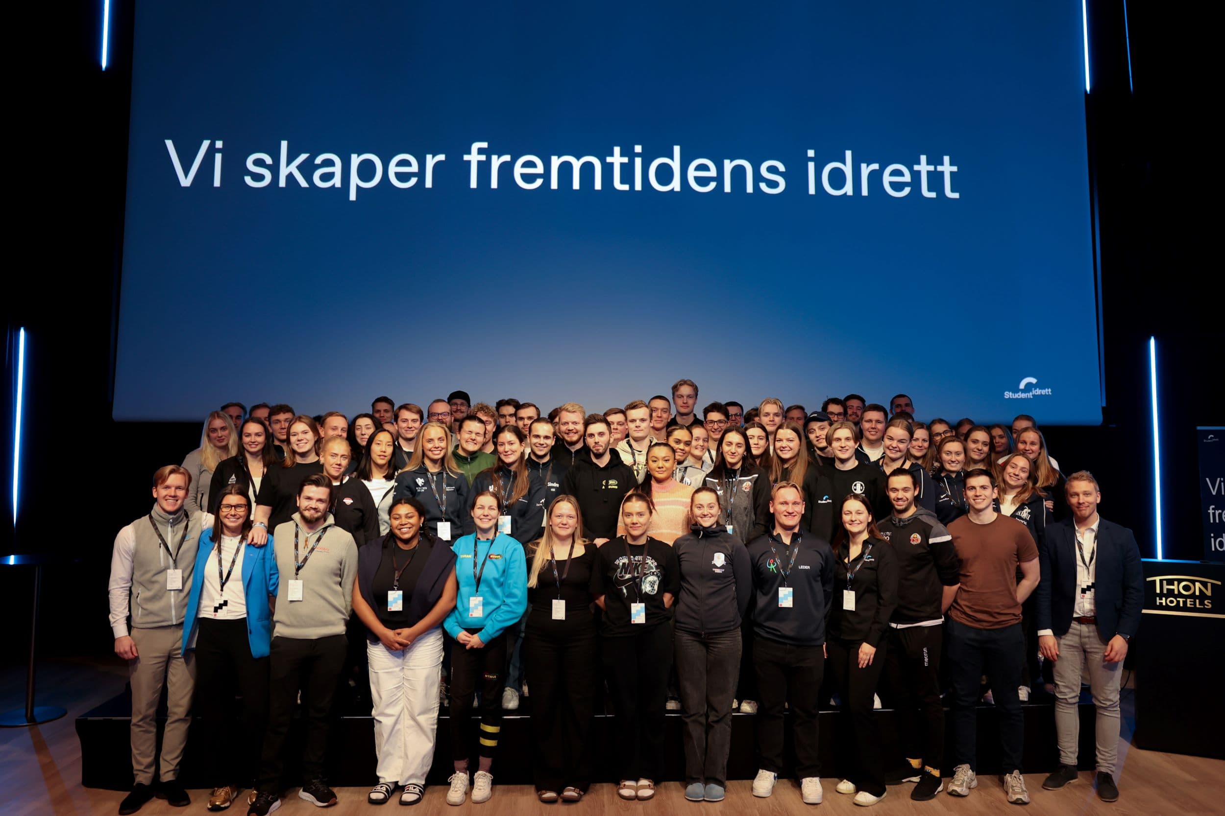 Stor gruppe deltakere samlet på en scene foran en skjerm med teksten «Vi skaper fremtidens idrett».