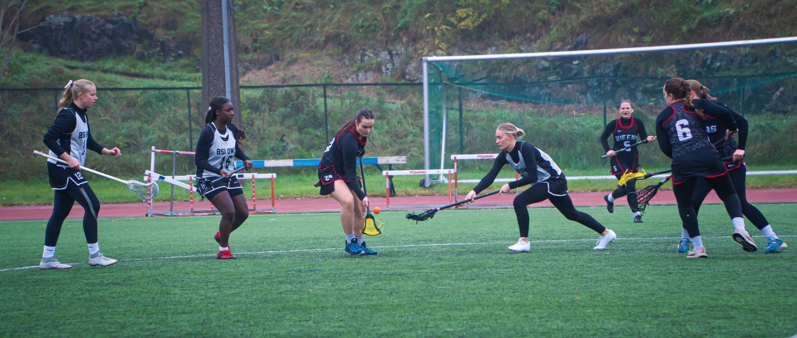 En gruppe kvinner spiller lacrosse med køller på en kunstgressbane.