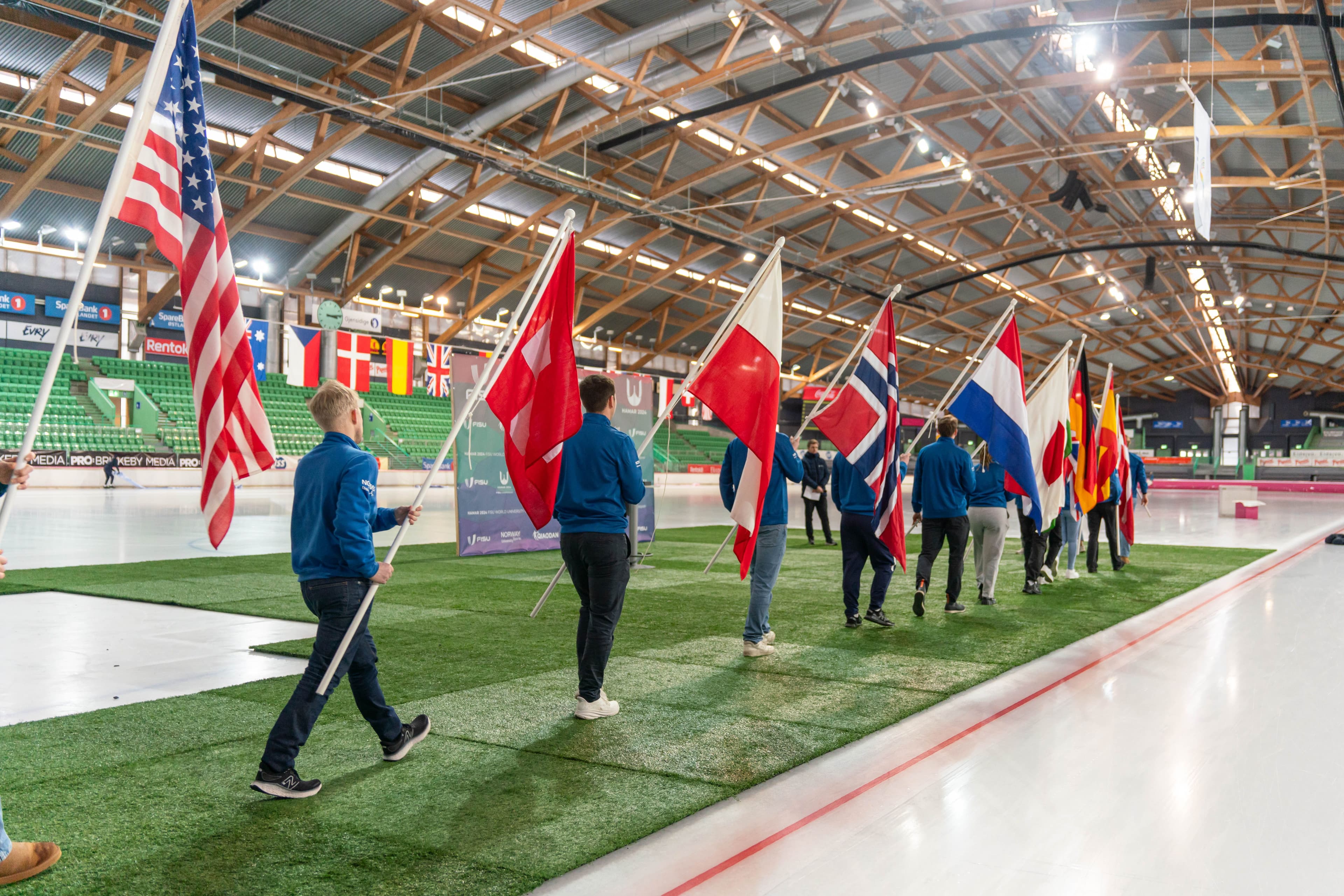 En rekke fanebærere med nasjonsflagg går inn på en skøytebane under en åpningsseremoni.
