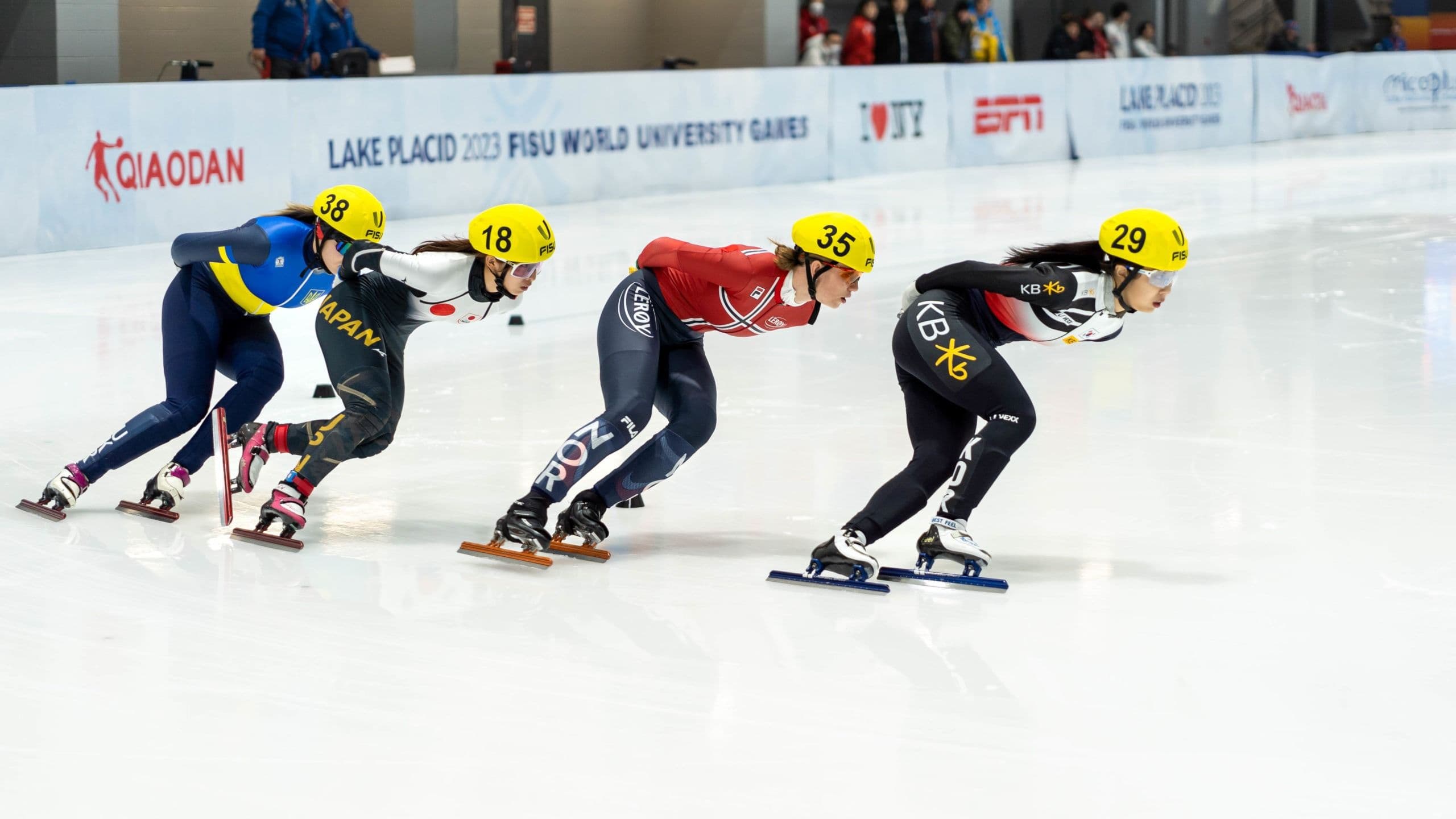 Fire kvinnelige shorttrack-skøyteløpere i sving på isbanen under FISU World University Games i Lake Placid.