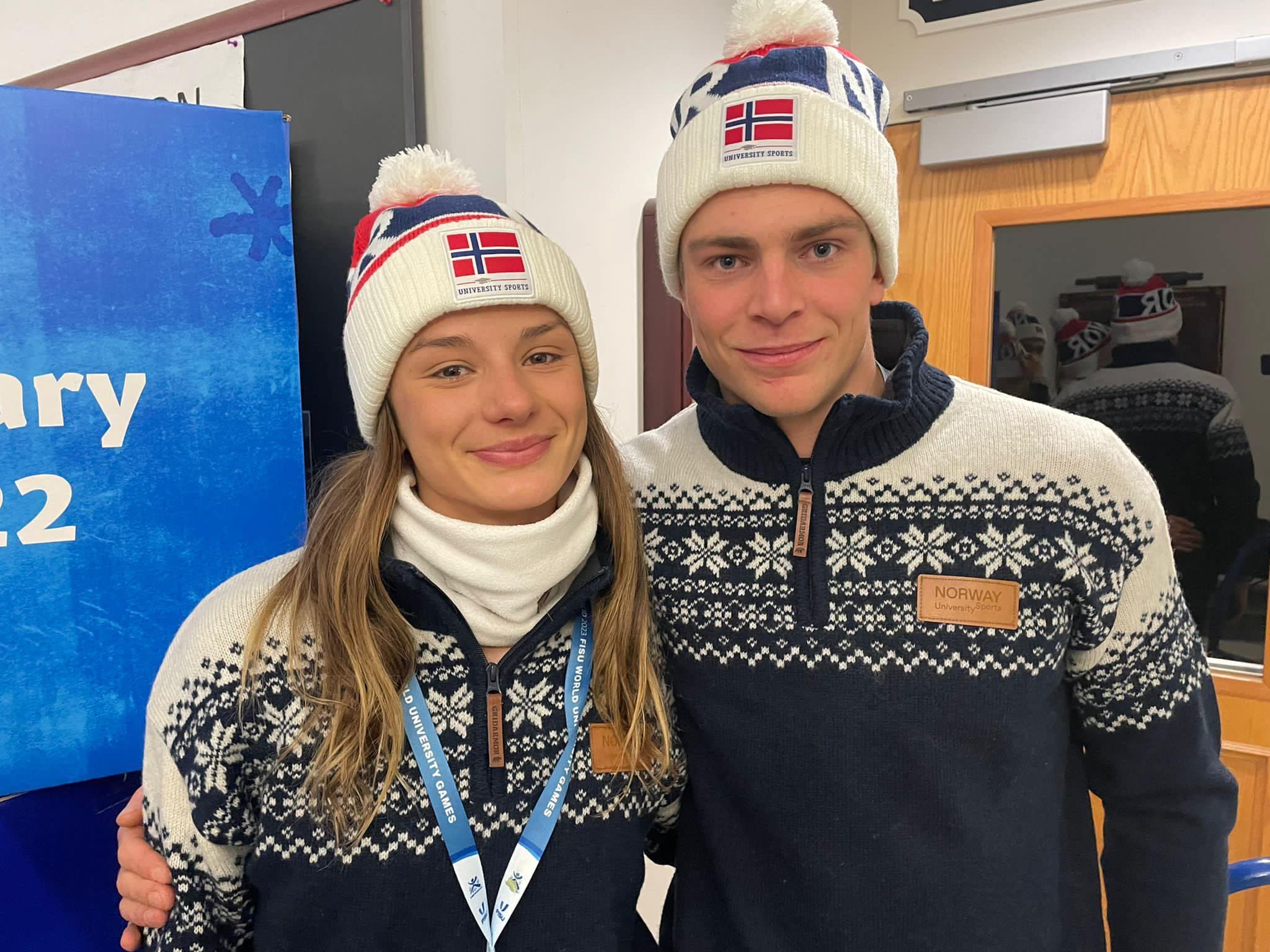 En kvinne og en mann i norske mønstergensere og luer med norsk flagg poserer sammen innendørs.