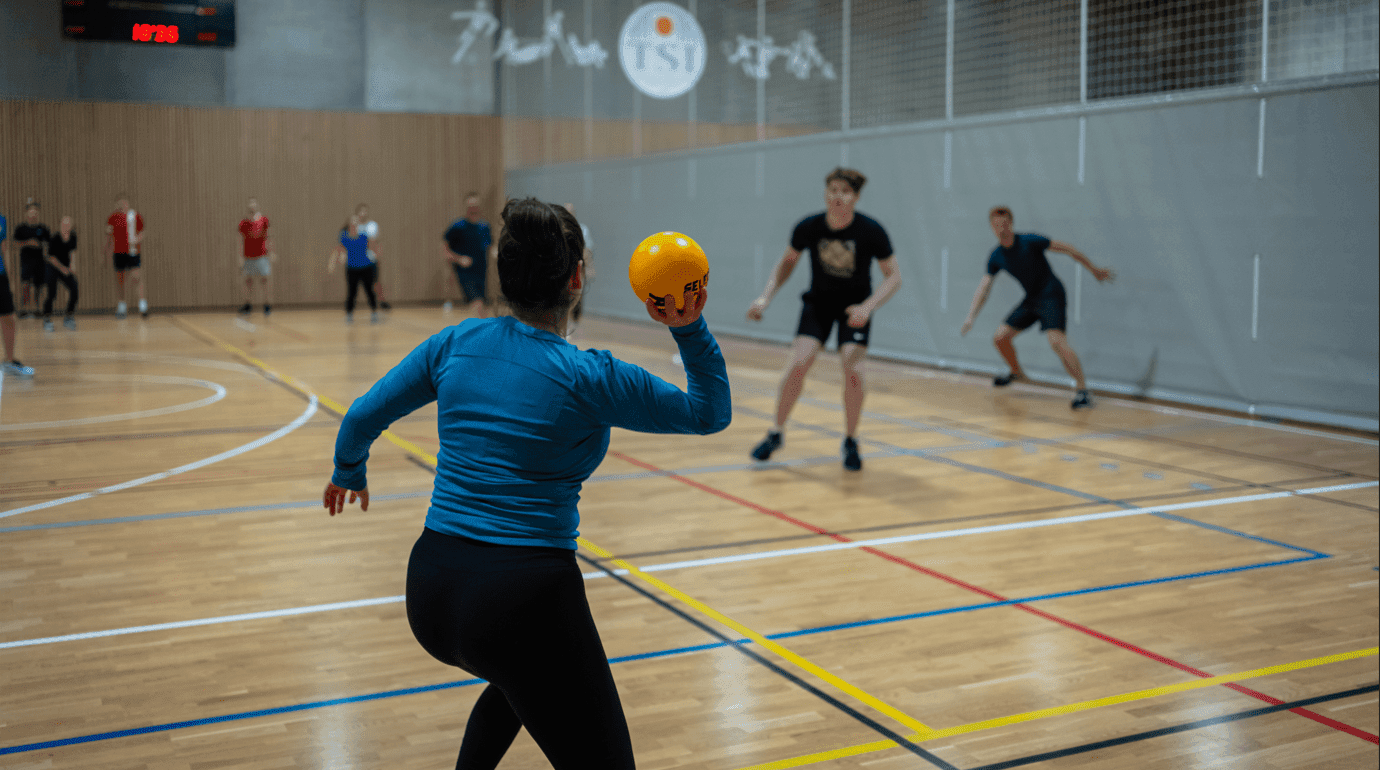 En kvinne kaster en oransje ball under et kanonballspill i en idrettshall.