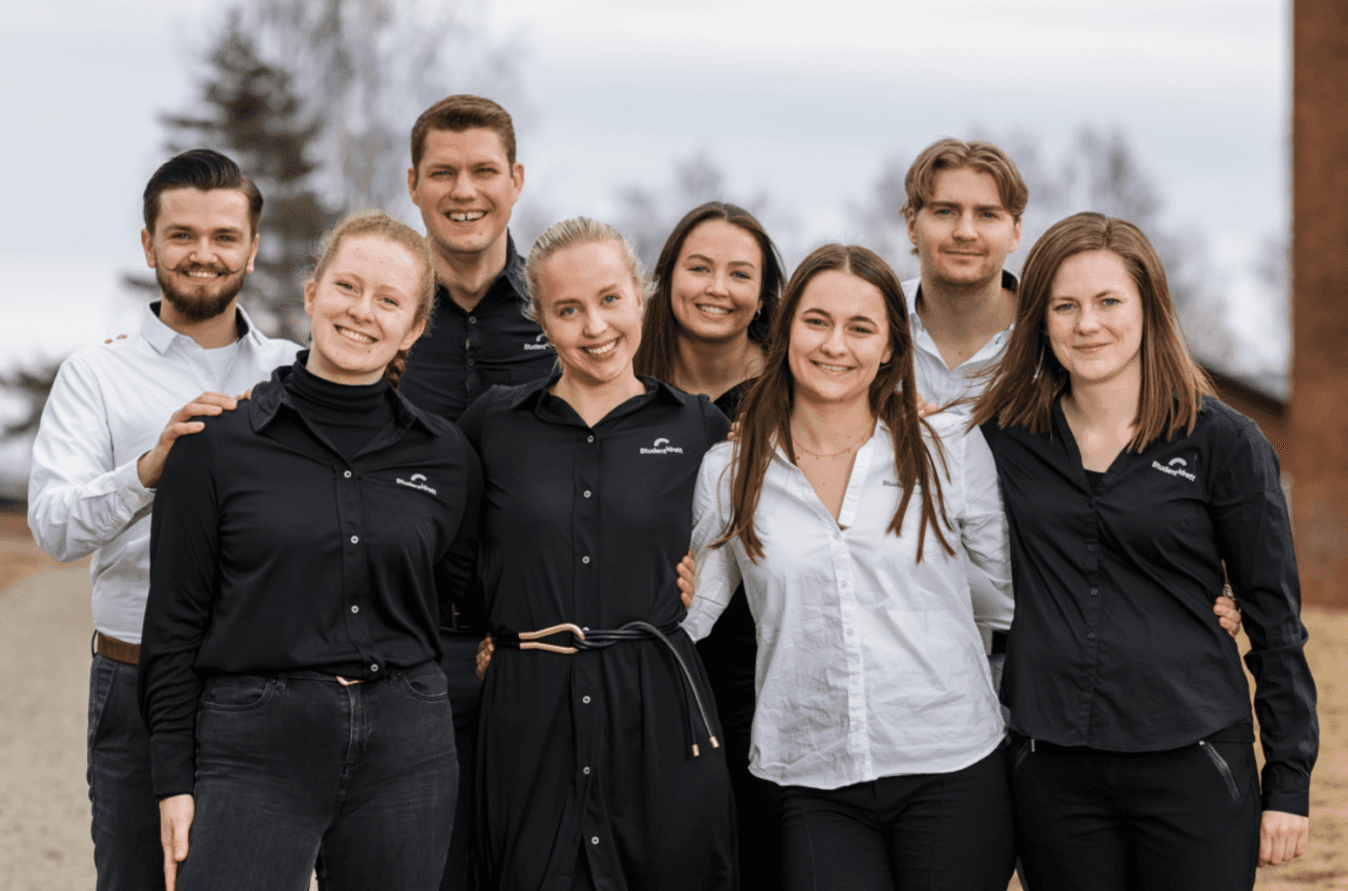 Gruppeportrett av åtte unge personer i sorte og hvite skjorter utendørs.
