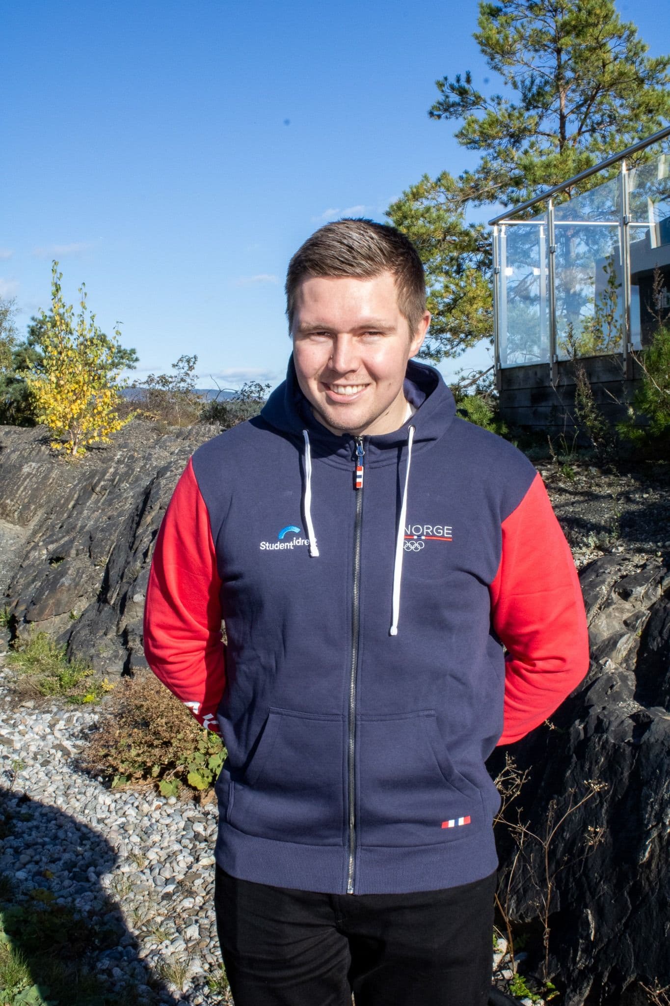 Portrett av en mann i Studentidrett- og Norge-genser utendørs på en solrik dag.