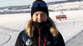 Portrett av en kvinne med lue og solbriller i vinterklær i et snødekt landskap.