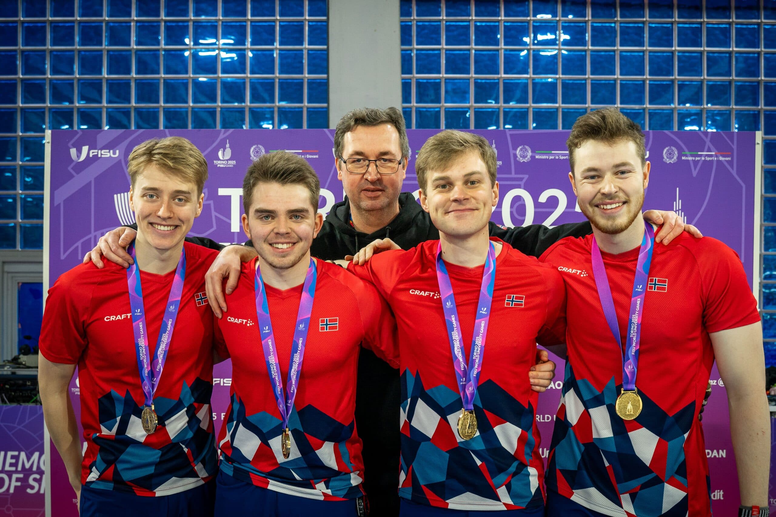 Fire mannlige utøvere i røde landslagsdrakter med medaljer poserer sammen med en trener på et FISU-mesterskap.