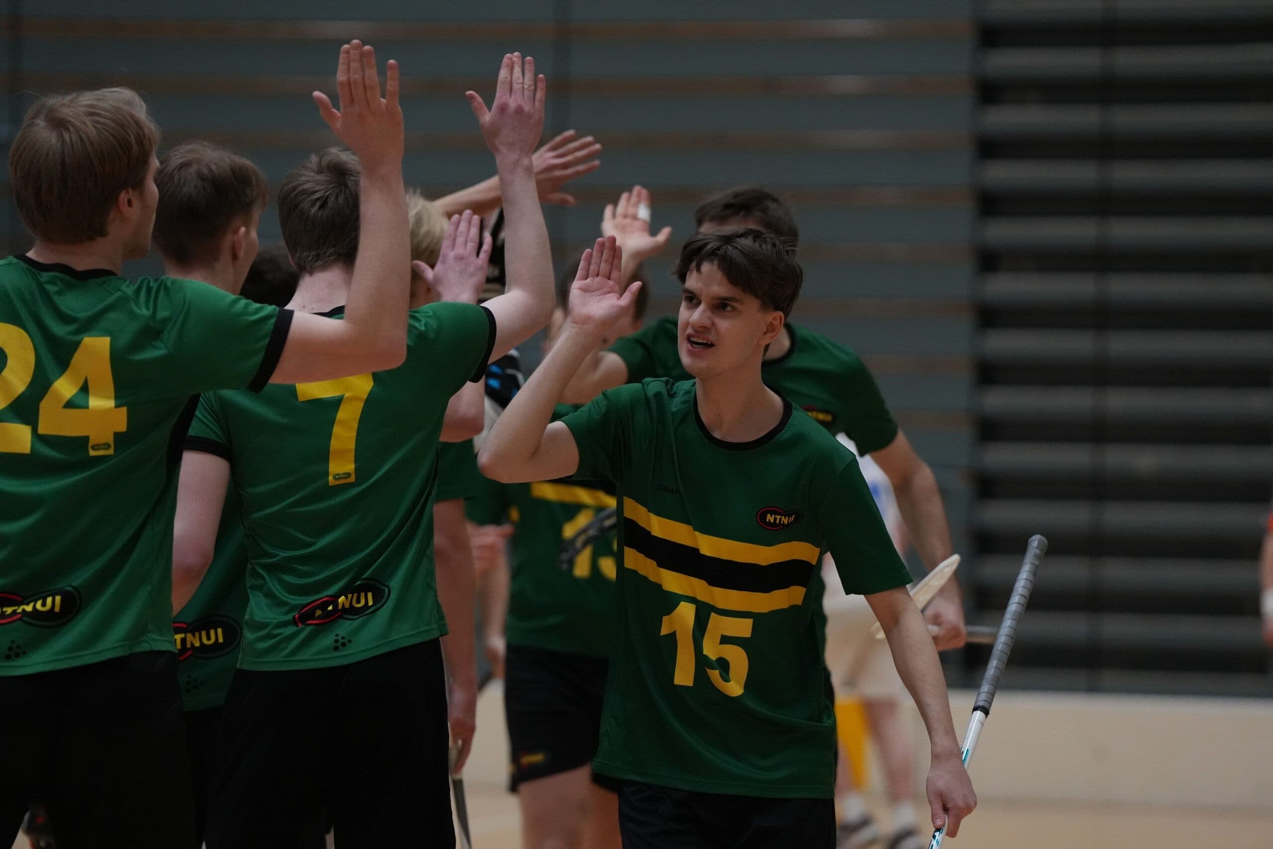 Badmintonspillere i grønne drakter gir hverandre high five i en idrettshall.