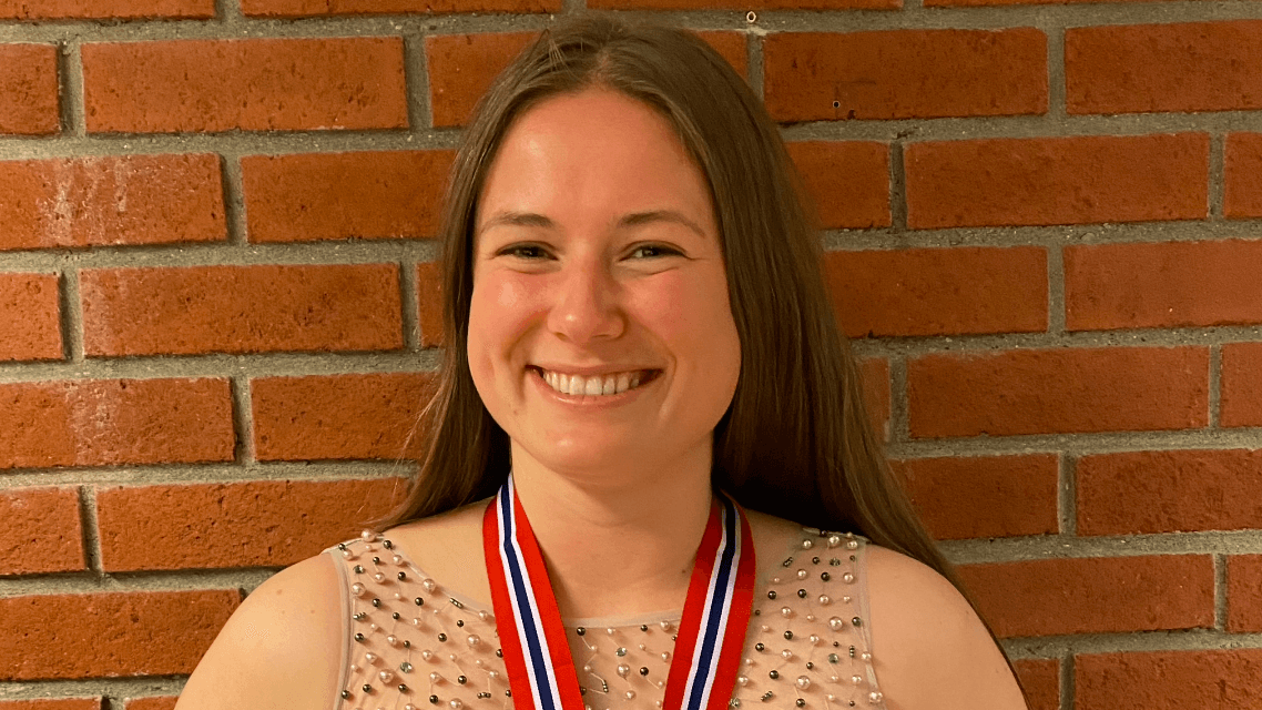 Portrett av en smilende kvinne med en medalje rundt halsen foran en teglsteinsvegg.