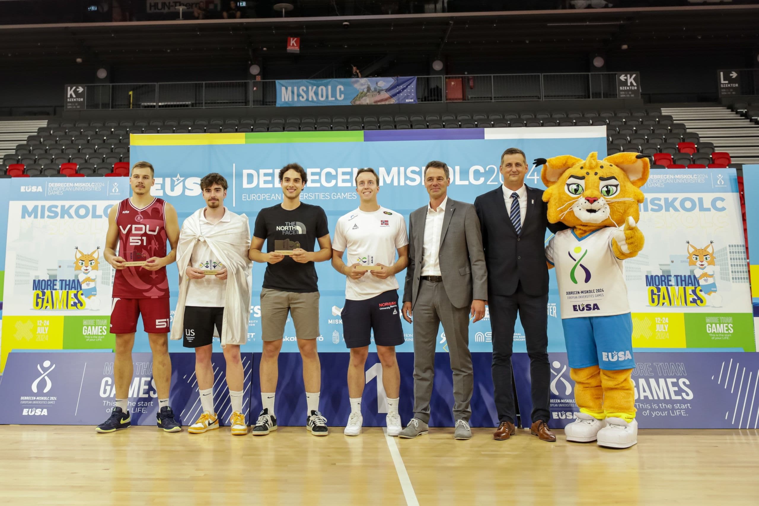 Fire basketballspillere med premier står sammen med arrangører og en maskot under en prisutdeling i Miskolc.