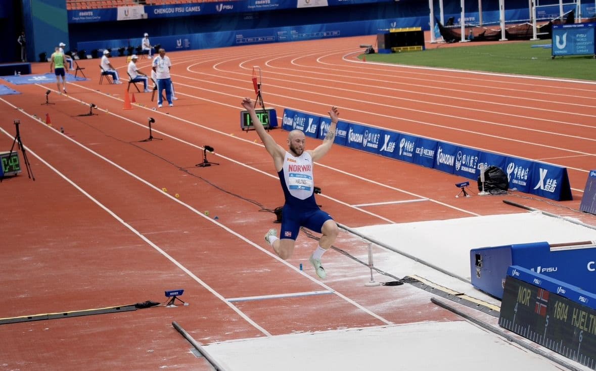 En utøver jubler med hevede armer i sandgropa på et friidrettsstadion under FISU-lekene.