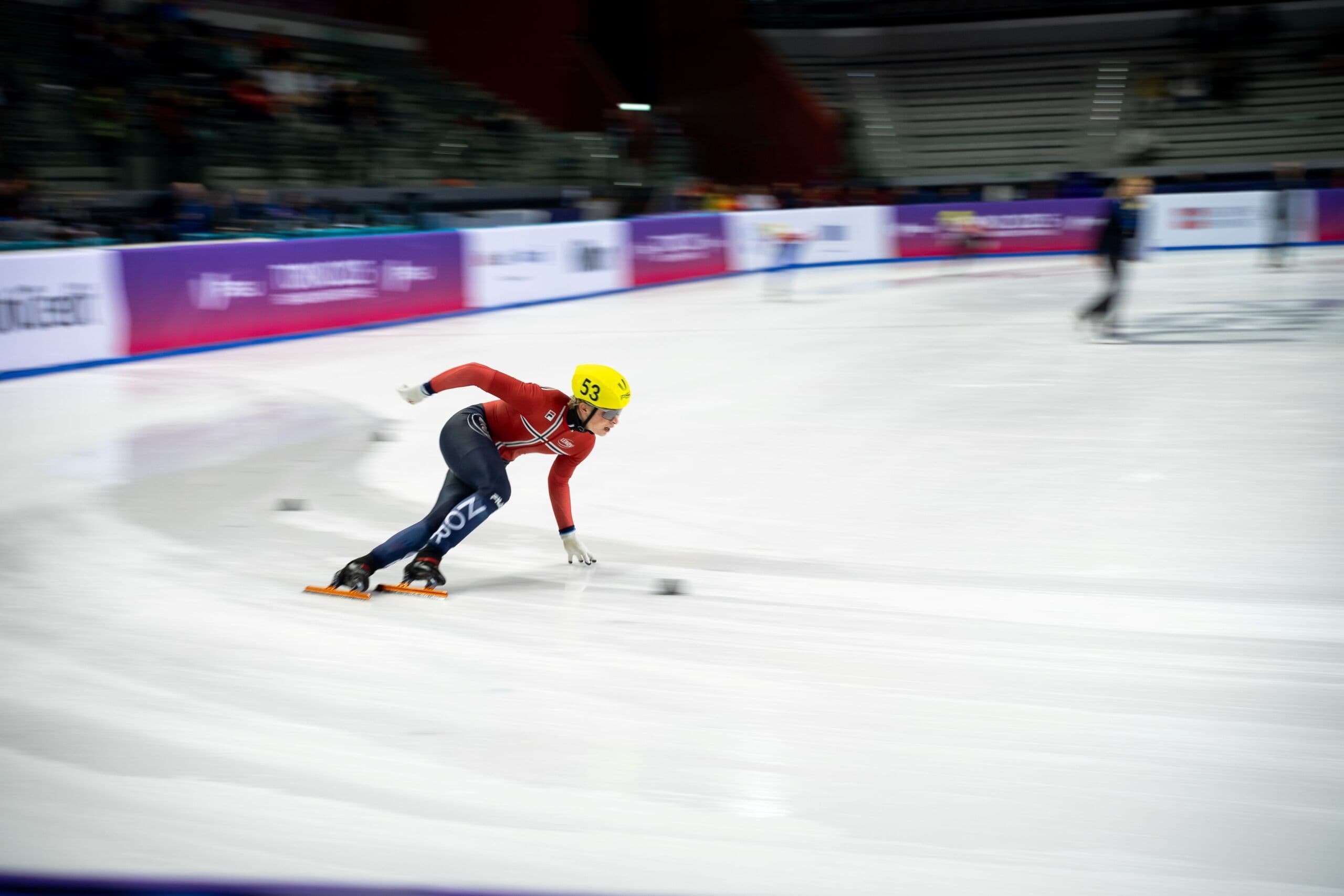 En skøyteløper i rød drakt med startnummer 33 kjører gjennom en sving i short track på isbanen.