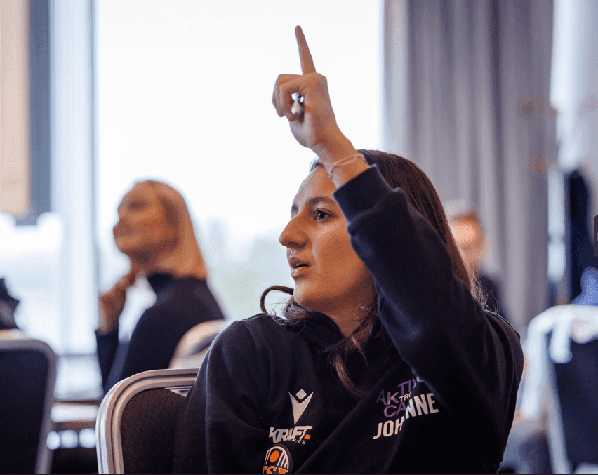 En ung kvinne rekker opp hånden for å ta ordet under et seminar.