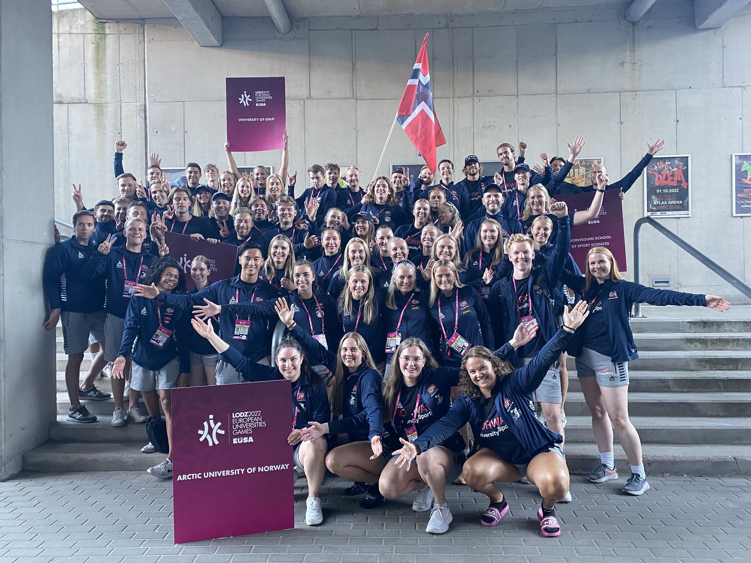 En stor delegasjon studenter i norske landslagsjakker poserer sammen med et norsk flagg.