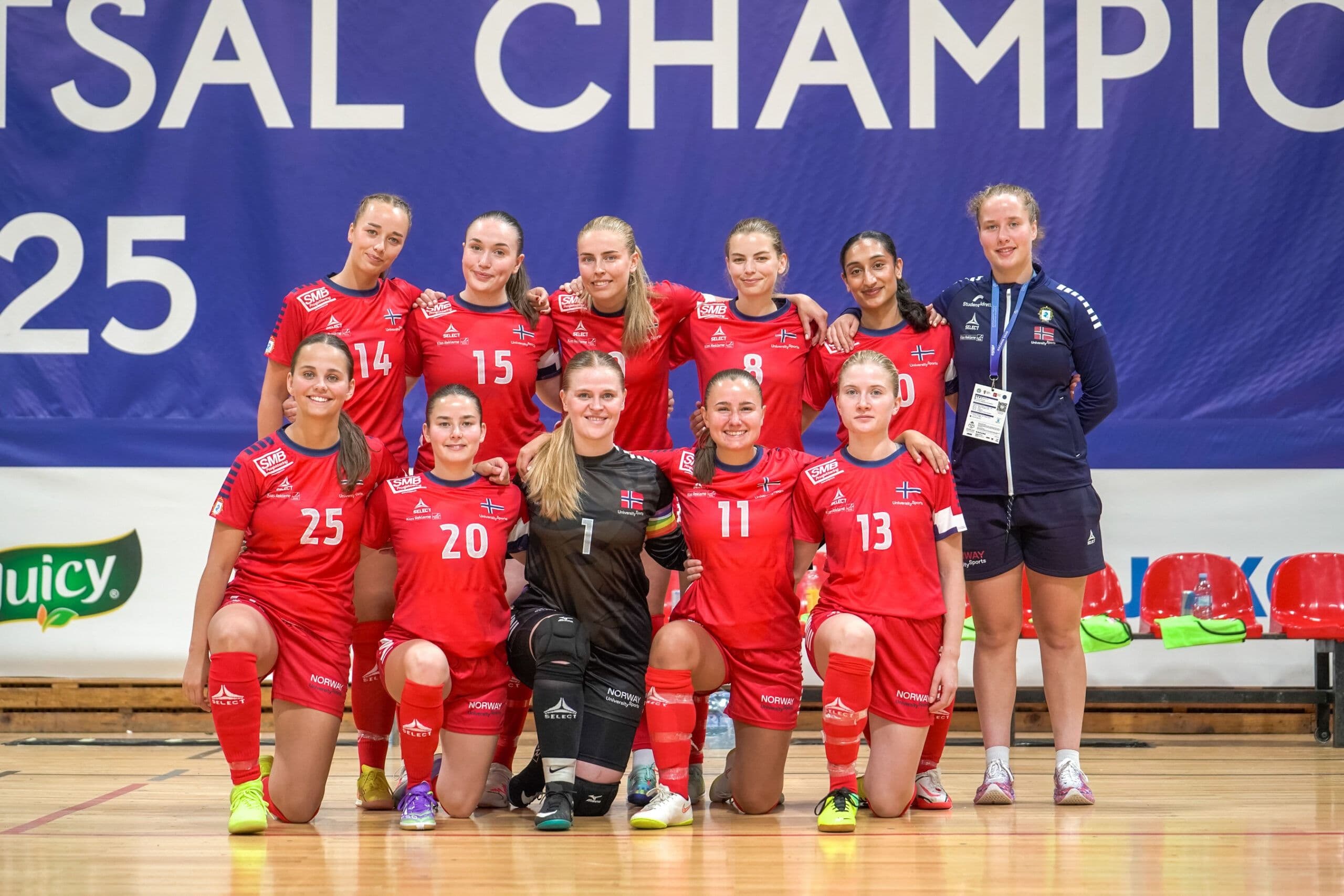 Et kvinnelig futsallag i røde drakter poserer for lagbilde foran et mesterskapsbanner.