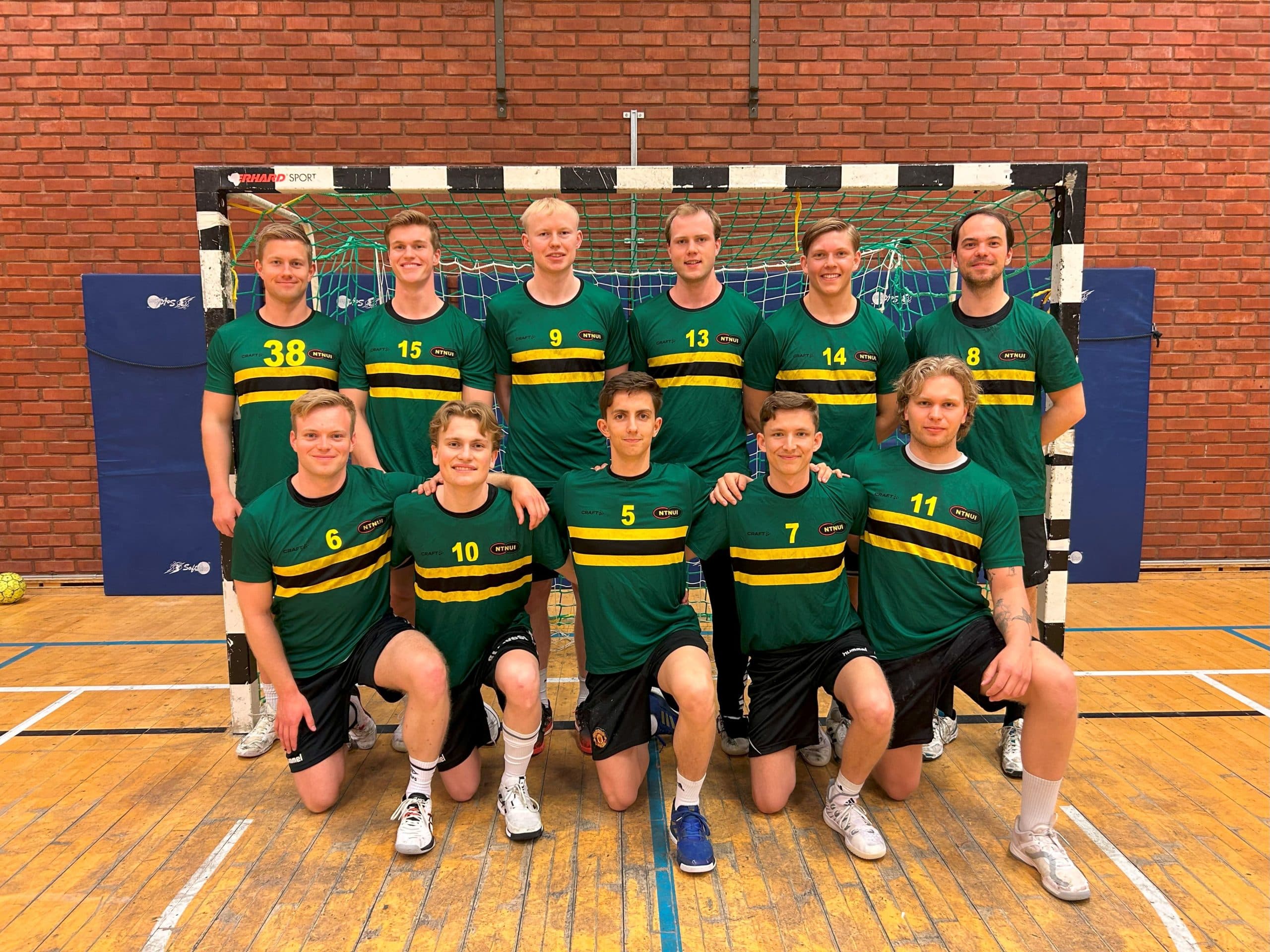 Et håndballag i grønne og gule drakter poserer for lagbilde foran målet i en hall.