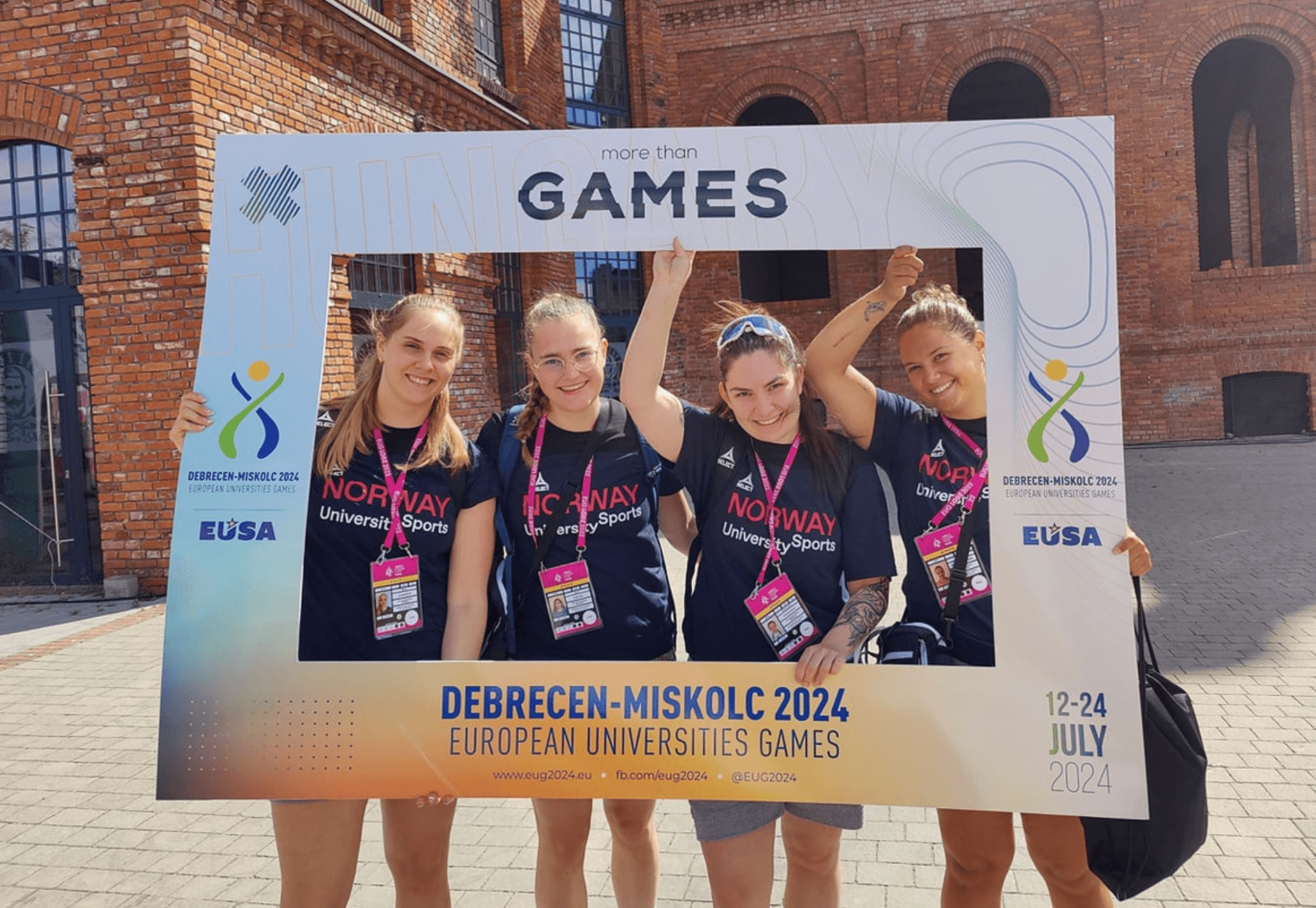 Fire kvinner poserer bak en fotoramme med teksten Debrecen-Miskolc 2024 European Universities Games.