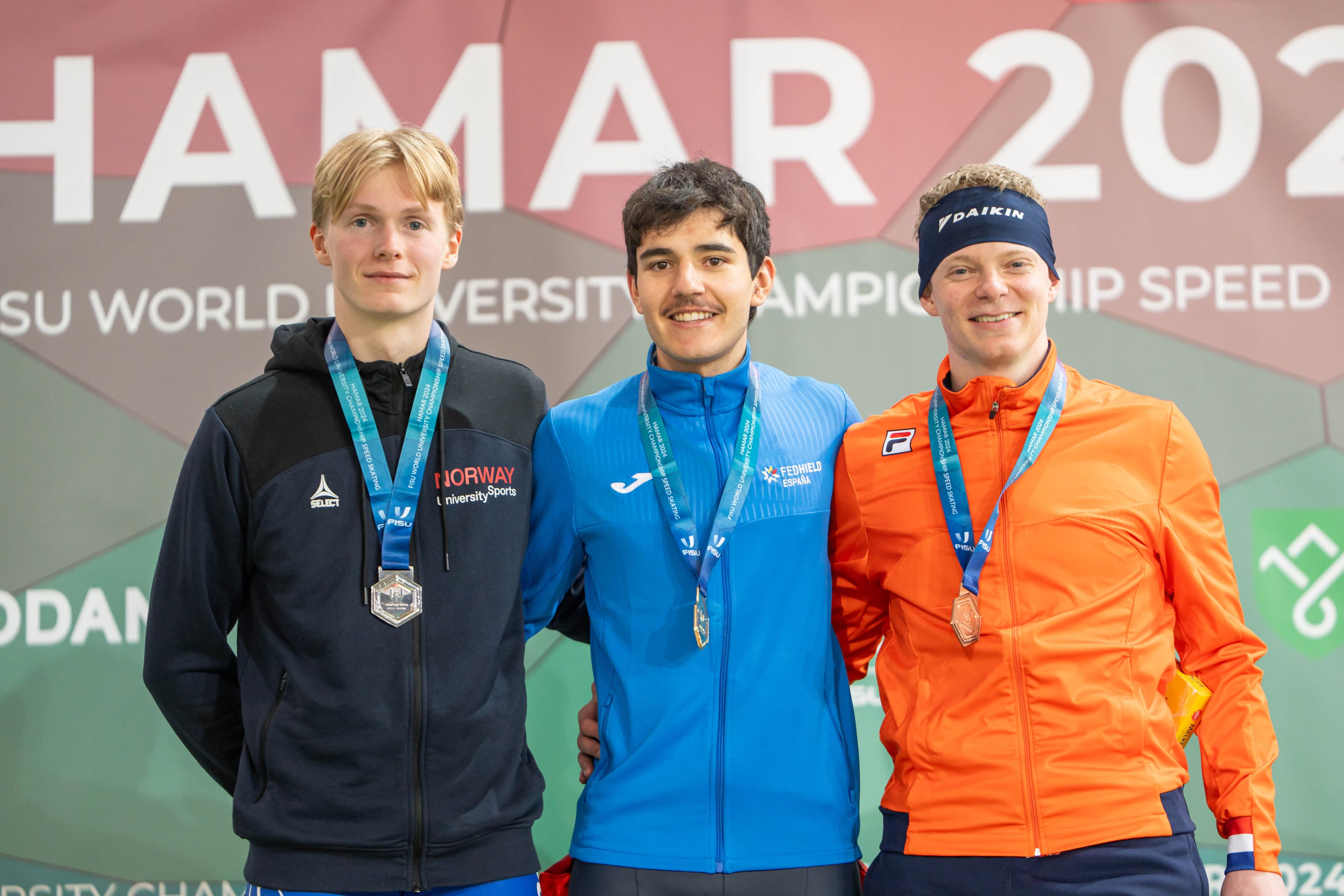 Tre mannlige skøyteløpere med medaljer på seierspallen foran en vegg med teksten Hamar 2024.