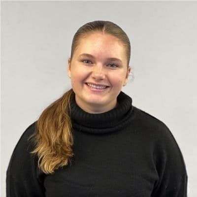 Portrett av en smilende kvinne i sort høyhalset genser mot lys bakgrunn.