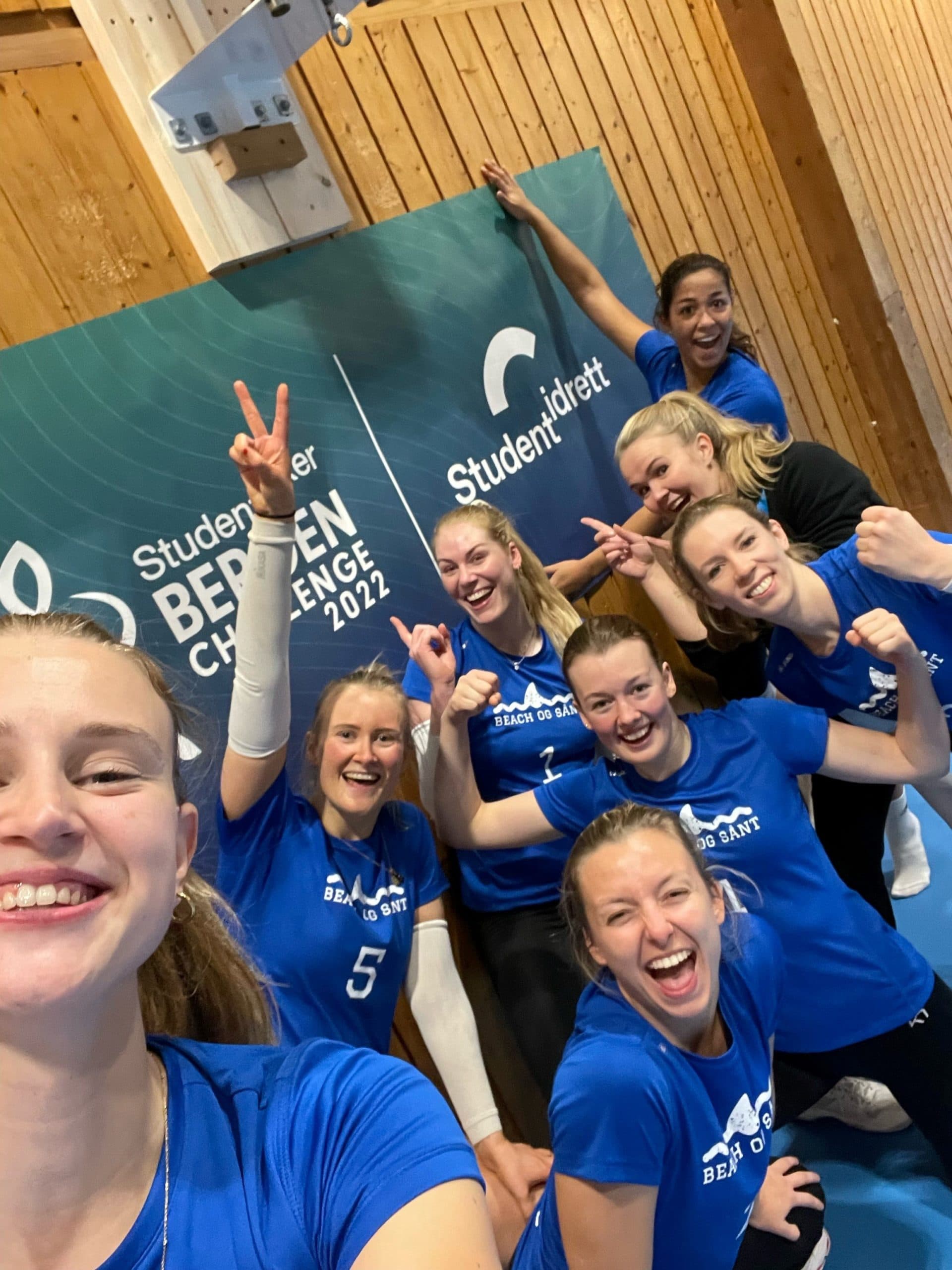 Et jublende kvinnelag i blå drakter tar en selfie foran en vegg med teksten Bergen Challenge 2022.