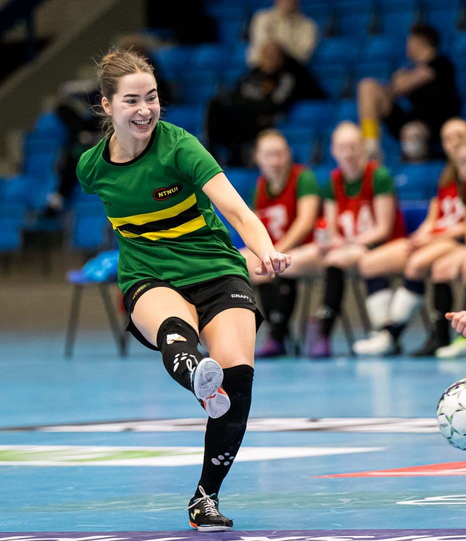 En futsalspiller i grønn NTNUI-drakt sparker ballen under en innendørskamp.