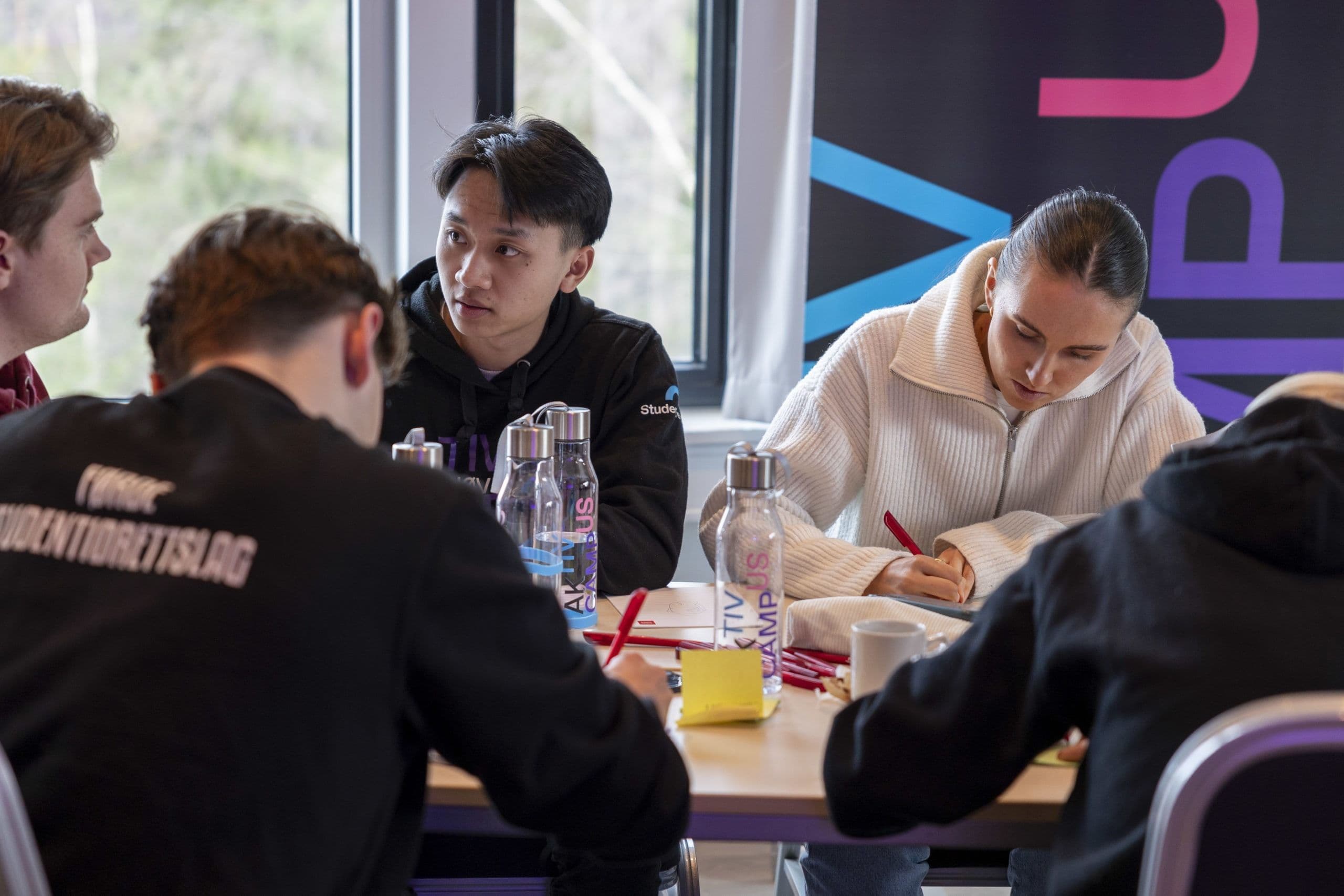 Fire studenter sitter og samarbeider rundt et bord på et Aktiv Campus-arrangement.
