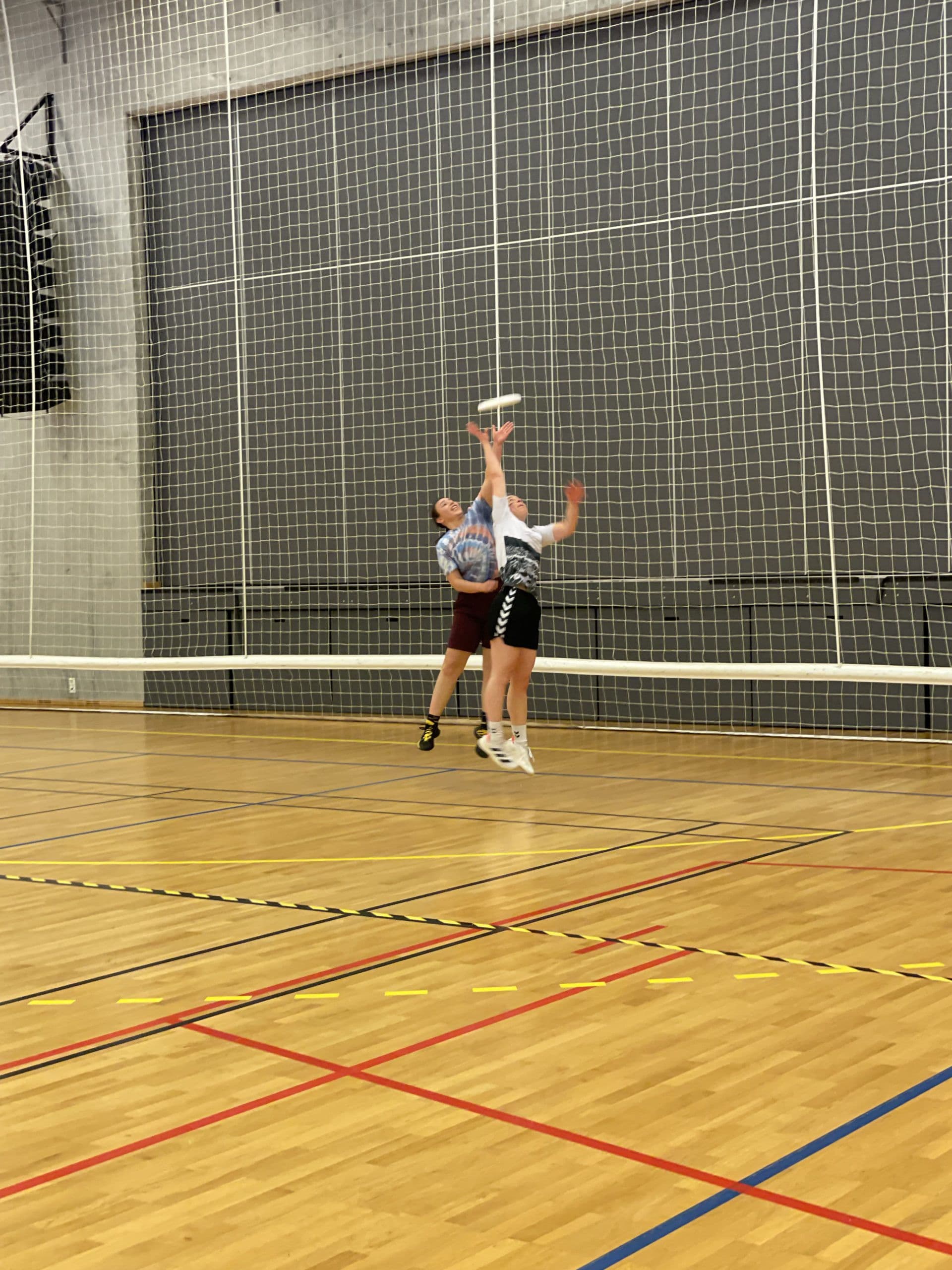 To spillere hopper opp etter en frisbee i en idrettshall under en ultimatekamp.