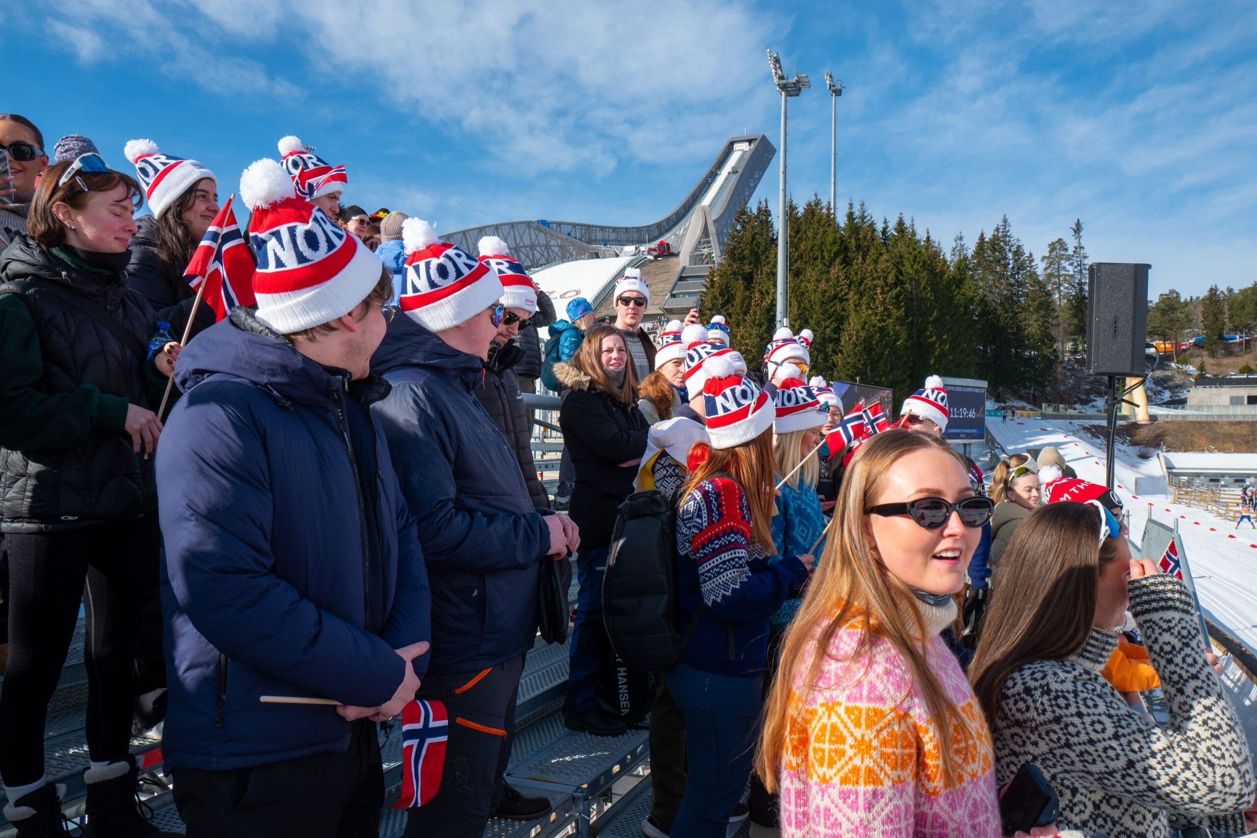 En gruppe studenter med norske flagg-luer foran Holmenkollen skihoppbakke.