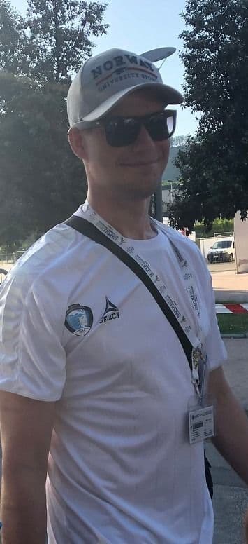 Portrett av en mann med caps, solbriller og akkreditering rundt halsen på et arrangement.