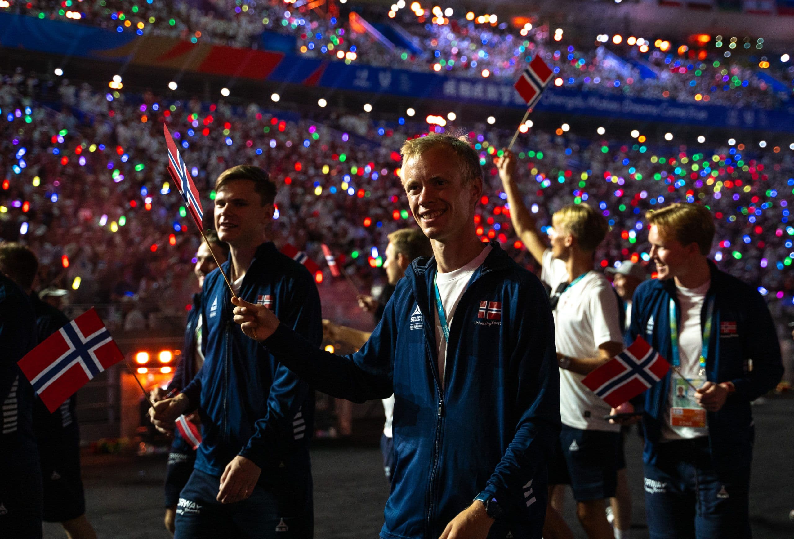 Den norske delegasjonen går inn med norske flagg under en åpningsseremoni på et stadion.