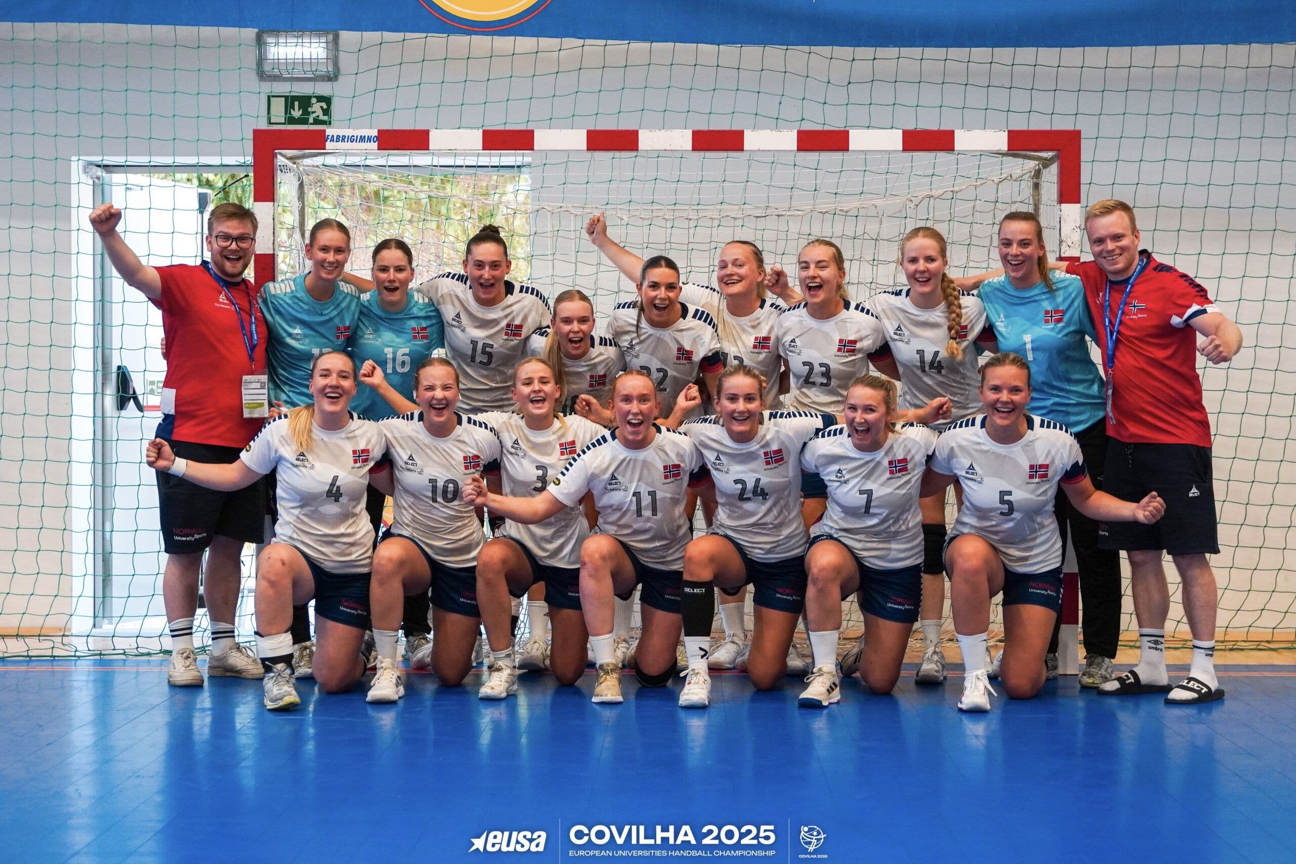 Et jublende håndball-damelag poserer foran målet i en idrettshall under EUSA Covilha 2025.