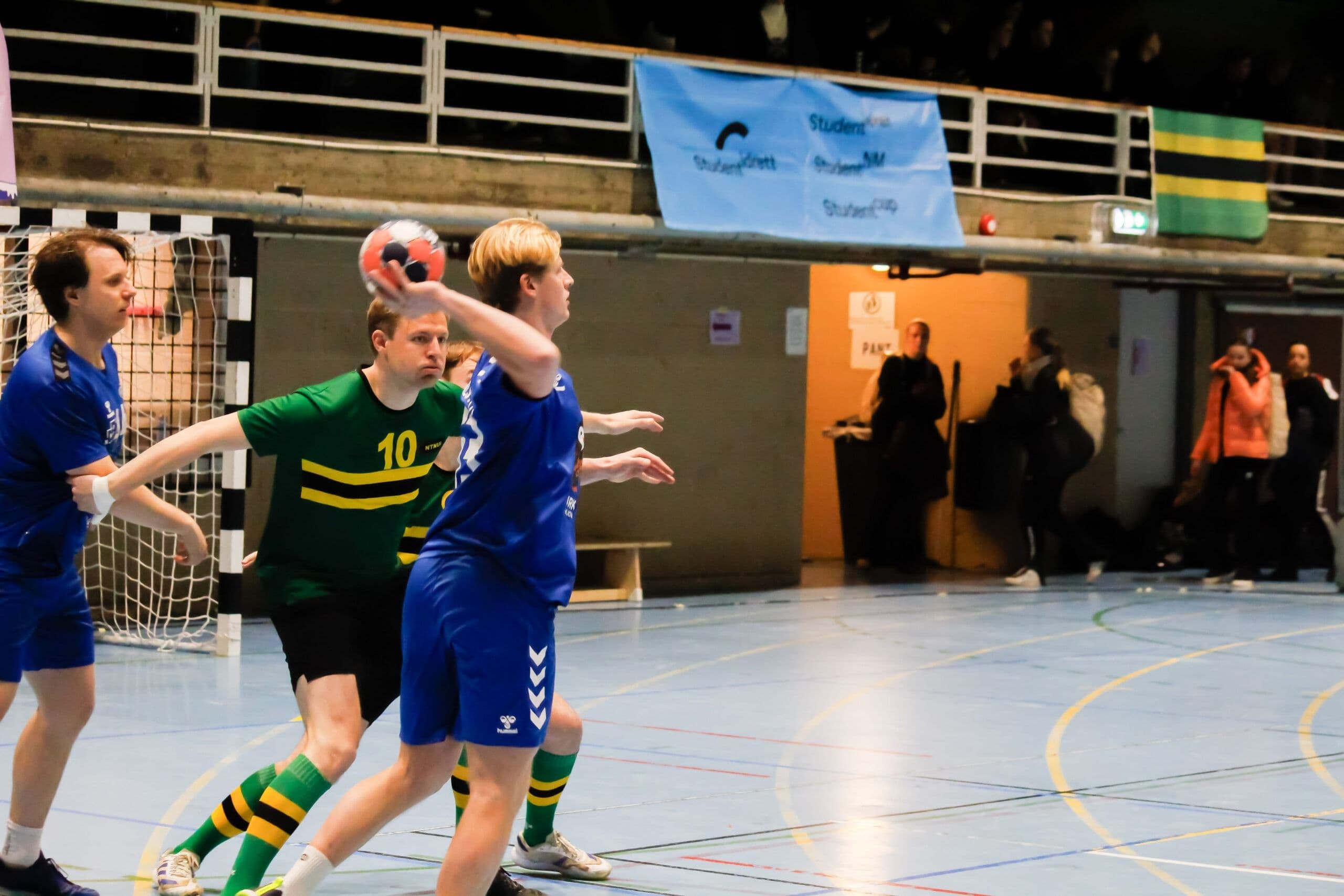 En håndballspiller i grønn drakt gjør seg klar til å kaste mens en motspiller i blått forsøker å stoppe henne.