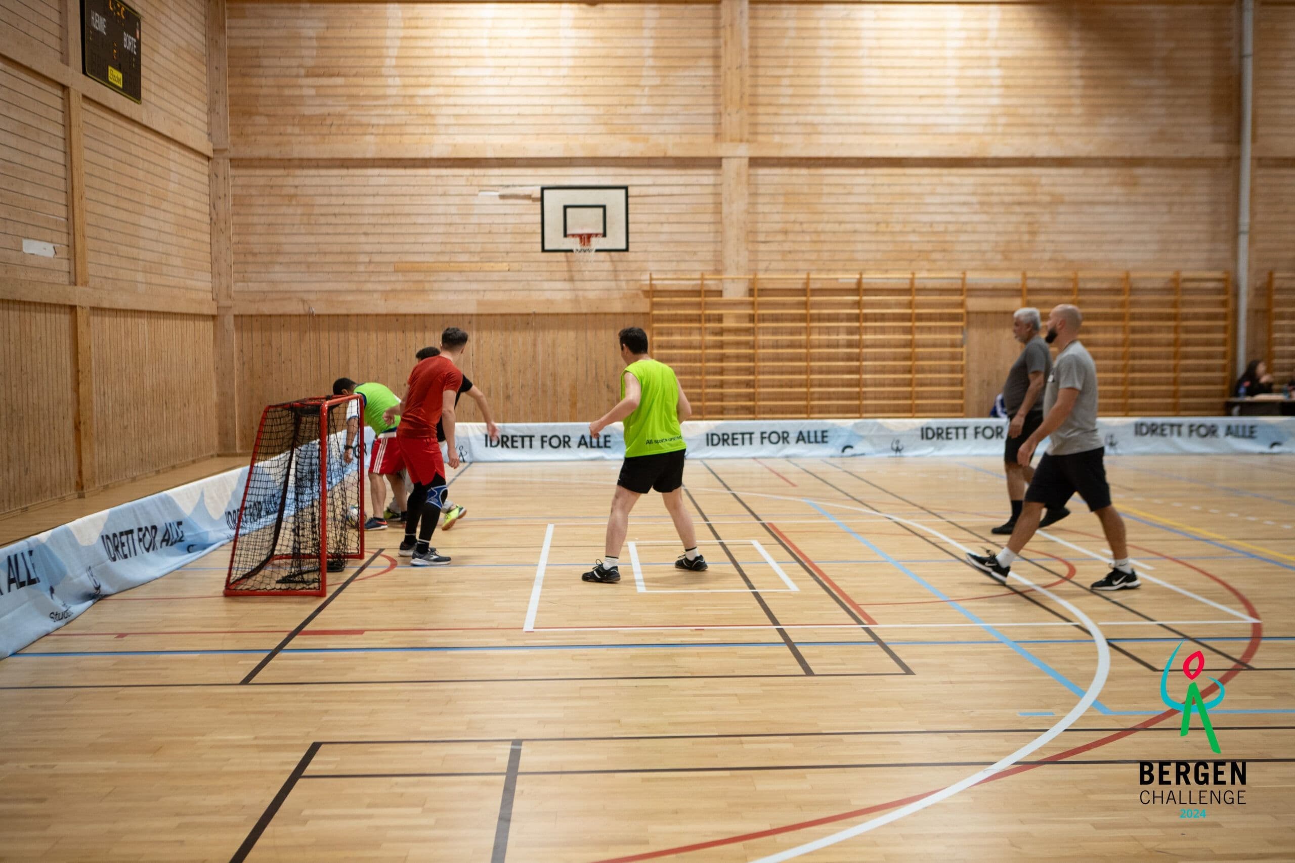 Personer spiller innebandy i en gymsal med bandereklame for Idrett for alle og logo for Bergen Challenge.