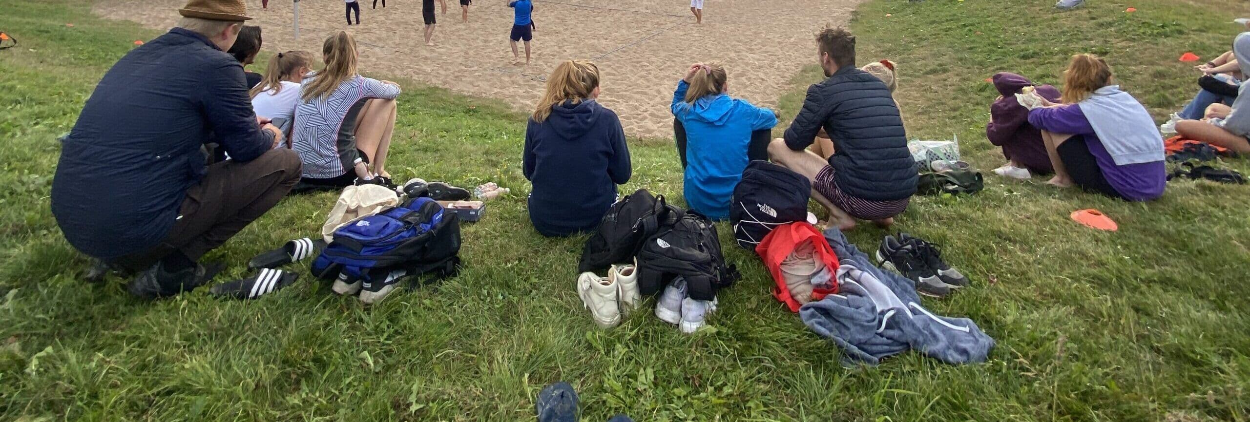 En gruppe studenter sitter i gresset med sekker ved siden av seg og ser utover et område.