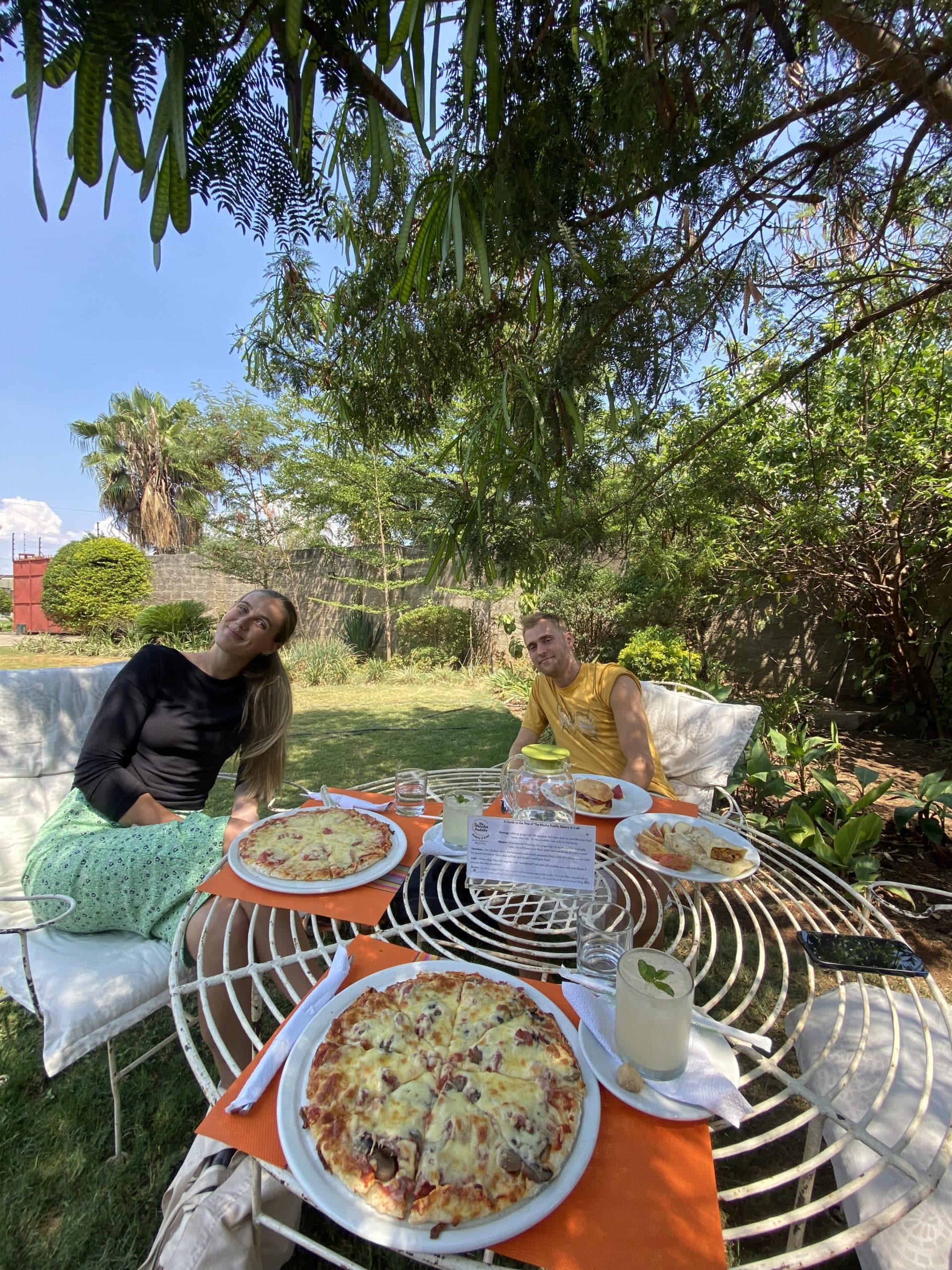 En kvinne og en mann sitter ved et hagebord dekket med pizza utendørs.