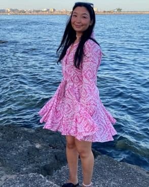 En kvinne i rosa mønstret kjole står ved vannkanten en solskinnsdag.