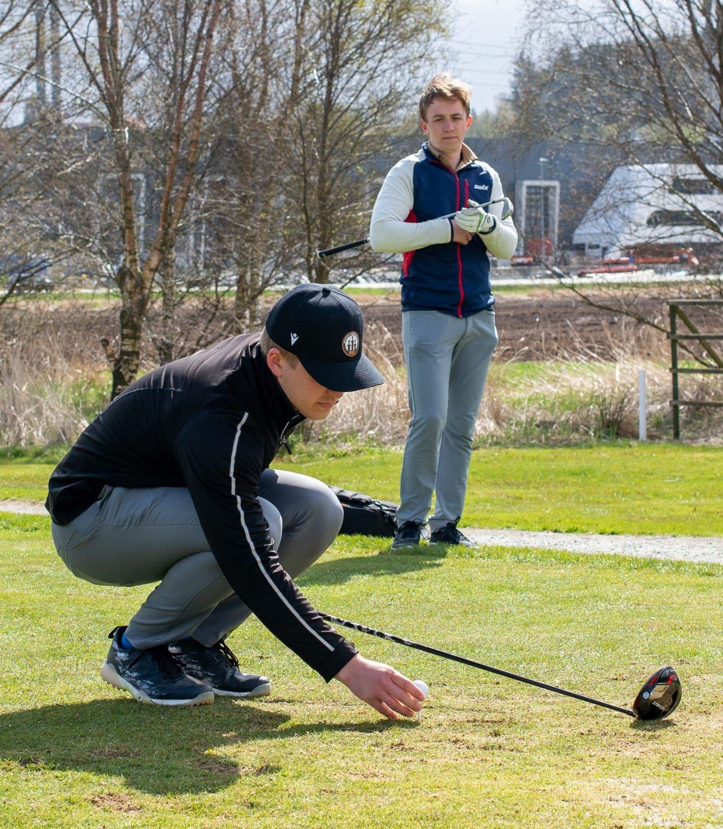 To golfspillere på en golfbane, den ene på huk for å plassere ballen mens den andre står og ser på.