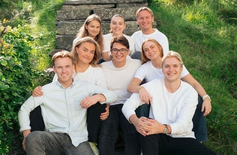 En gruppe unge studenter i hvite klær sitter samlet ute i naturen.