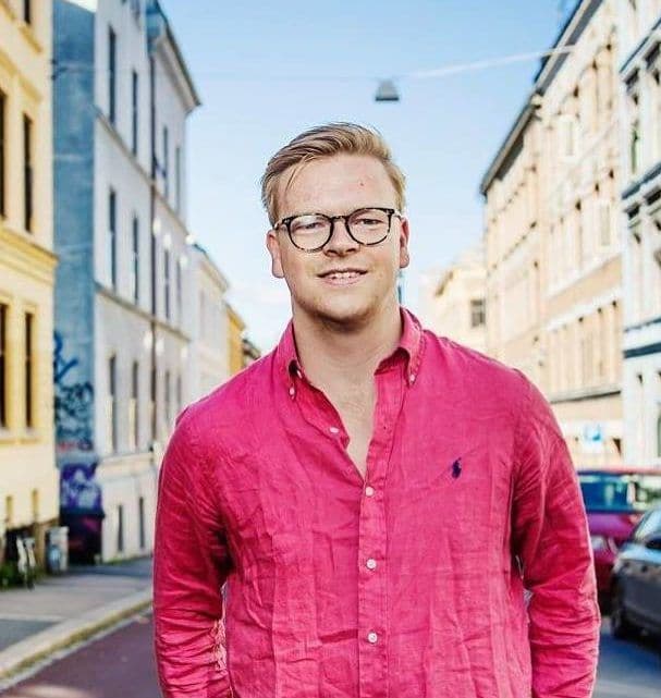 Portrett av en mann med briller og rosa skjorte i en bygate.