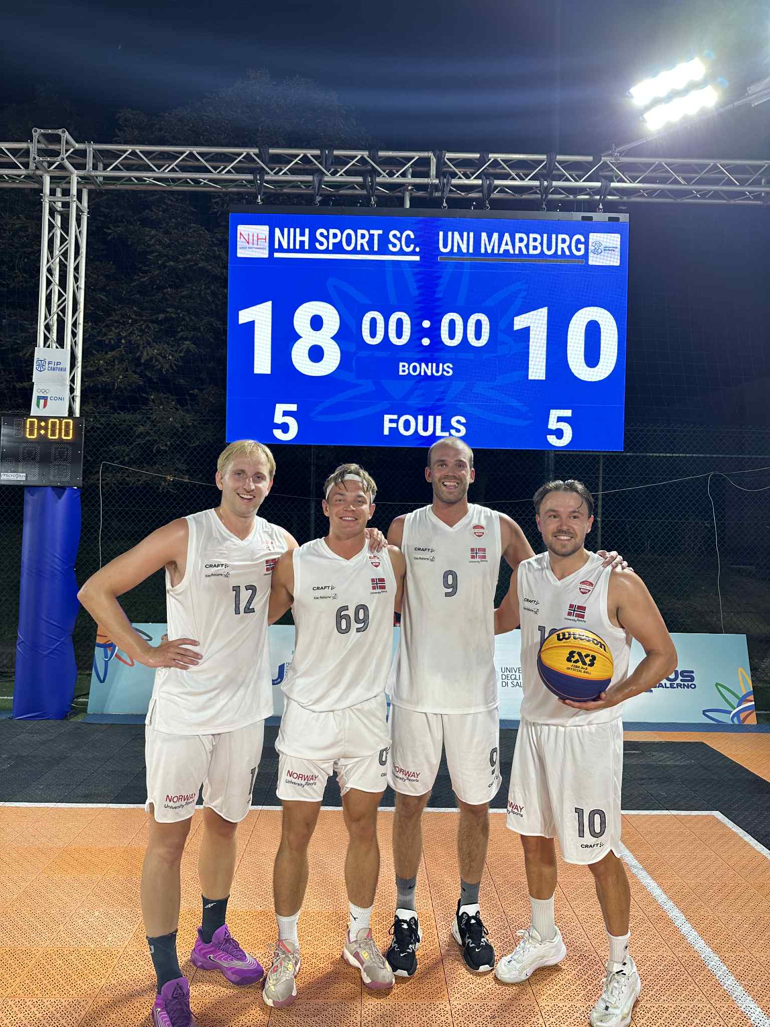 Fire basketballspillere i hvite drakter poserer foran en resultattavle etter en 3x3-kamp.