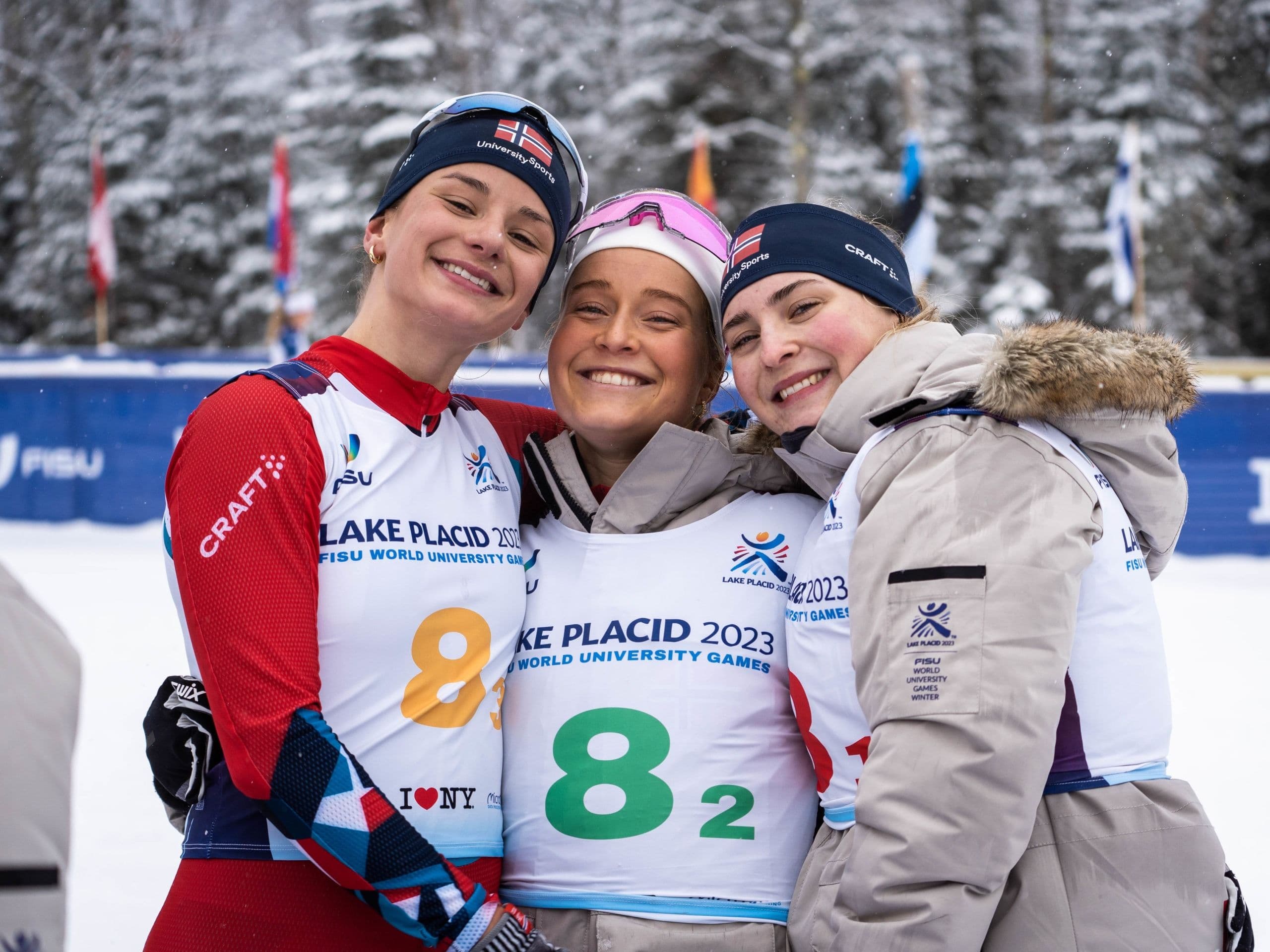 Tre kvinnelige langrennsutøvere klemmer hverandre og smiler etter et stafettløp i Lake Placid 2023.