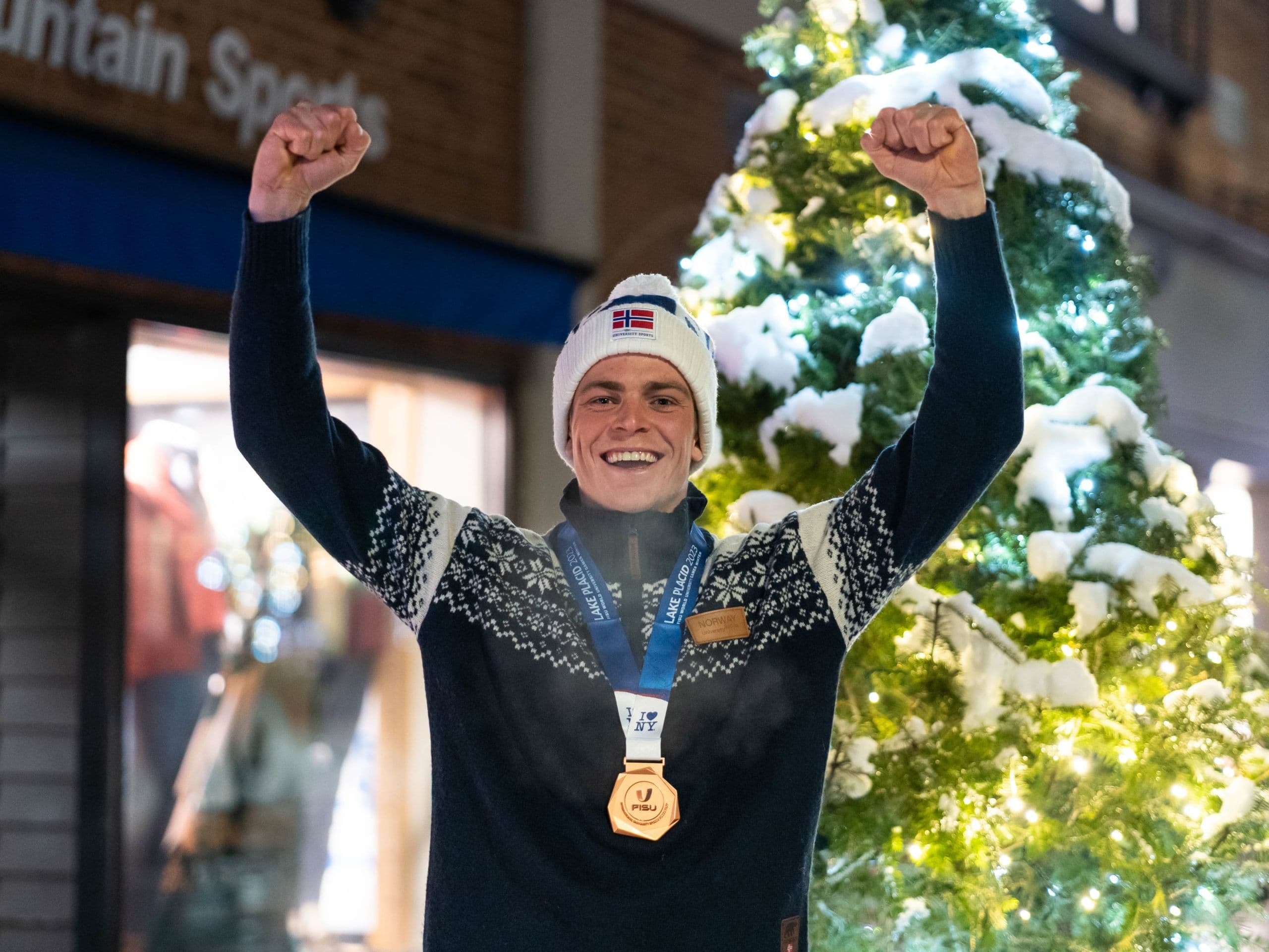 En mann jubler med en bronsemedalje rundt halsen foran et opplyst juletre.