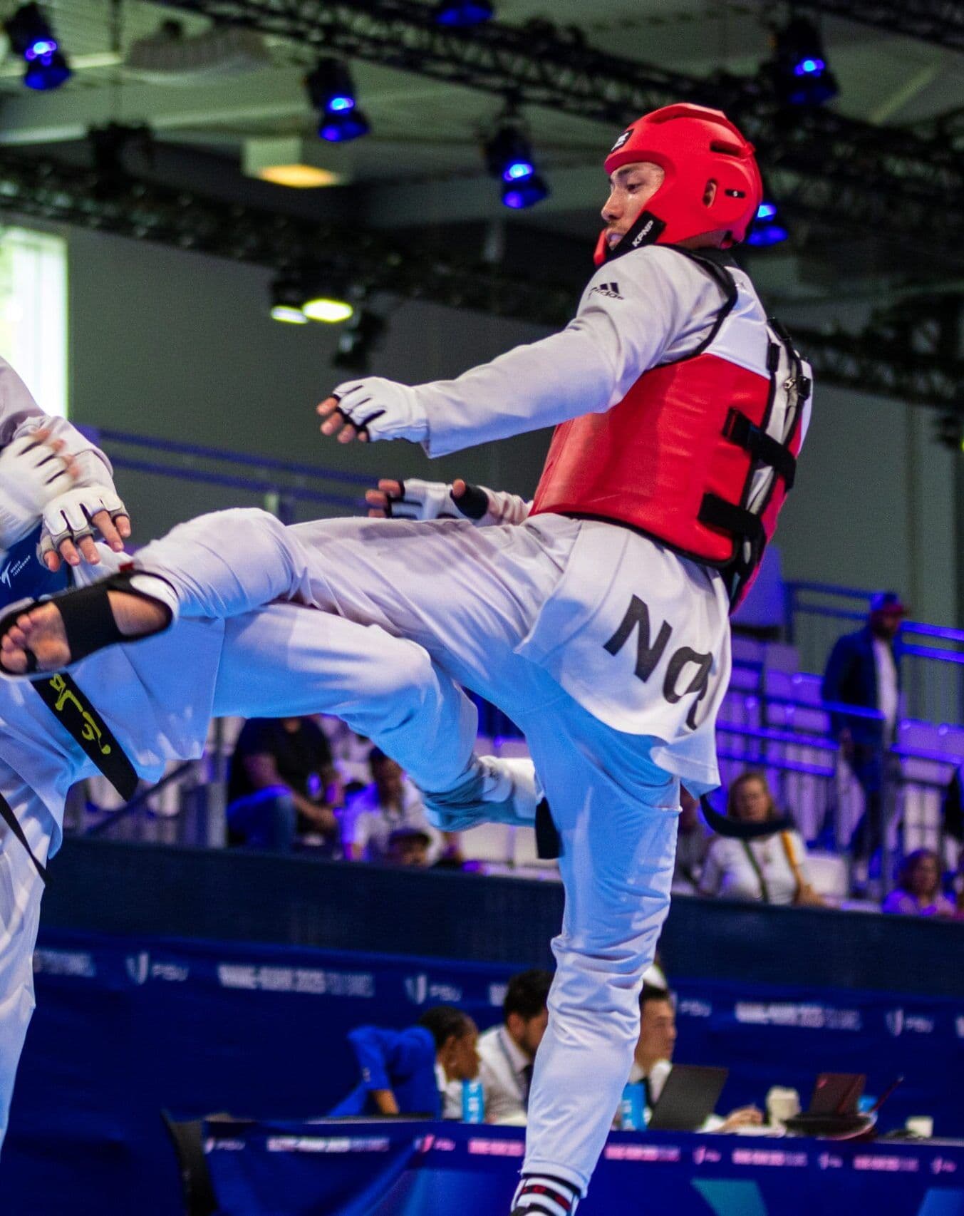 To taekwondo-utøvere i kamp, den ene med rødt hodevern og vest.