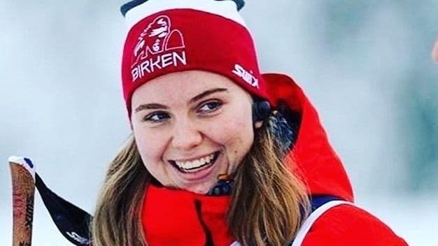 Portrett av en smilende kvinne med rød Birken-lue ute i vinterlandskap.