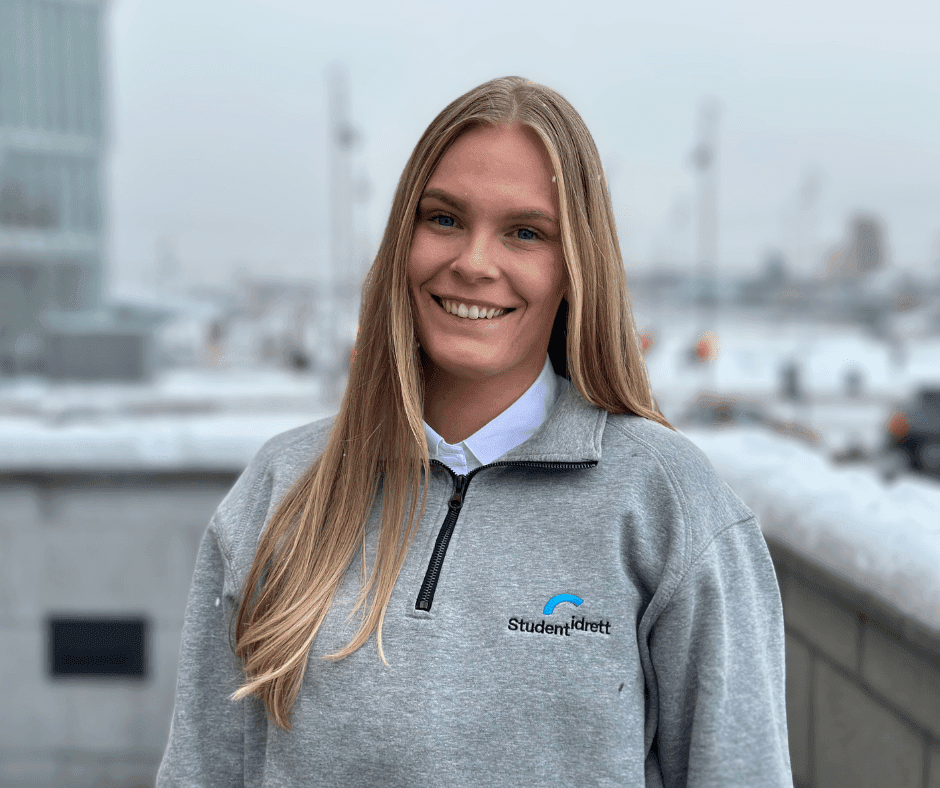 Portrett av en smilende kvinne i grå Studentidrett-genser utendørs om vinteren.