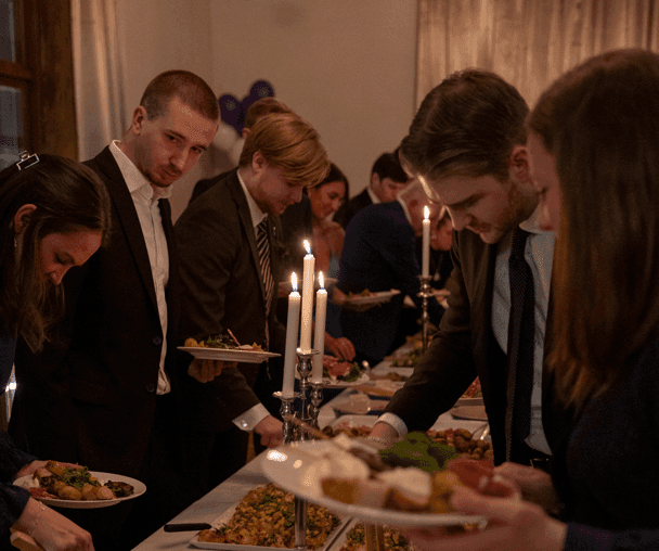 Festkledde personer forsyner seg fra et langbord med stearinlys under en middag.