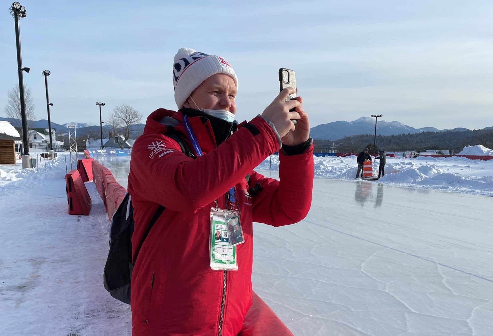 En person i rød jakke tar bilde med mobilen ved en utendørs skøytebane om vinteren.