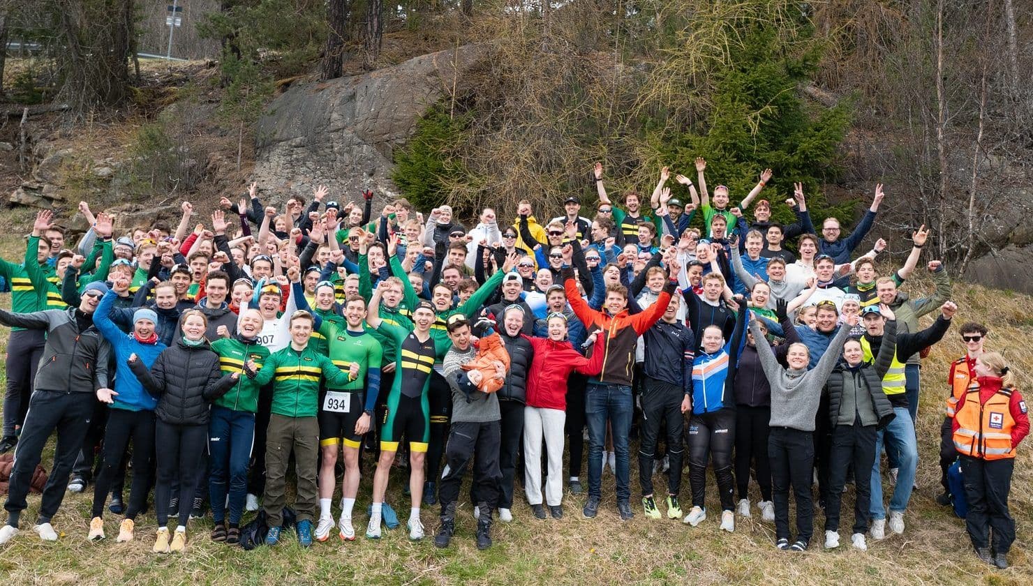 Kvinne i blå jakke og pannebånd med norsk flagg smiler foran et snødekt fjell.