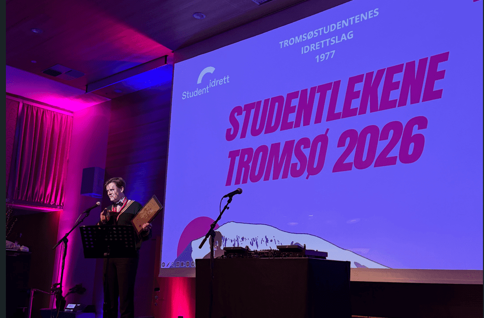 En person taler ved en talerstol foran en lerret med teksten Studentlekene Tromsø 2026.
