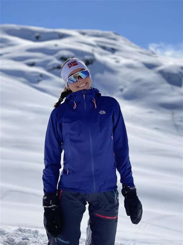 En kvinnelig lacrossespiller i lilla drakt løper etter ballen på en kunstgressbane.