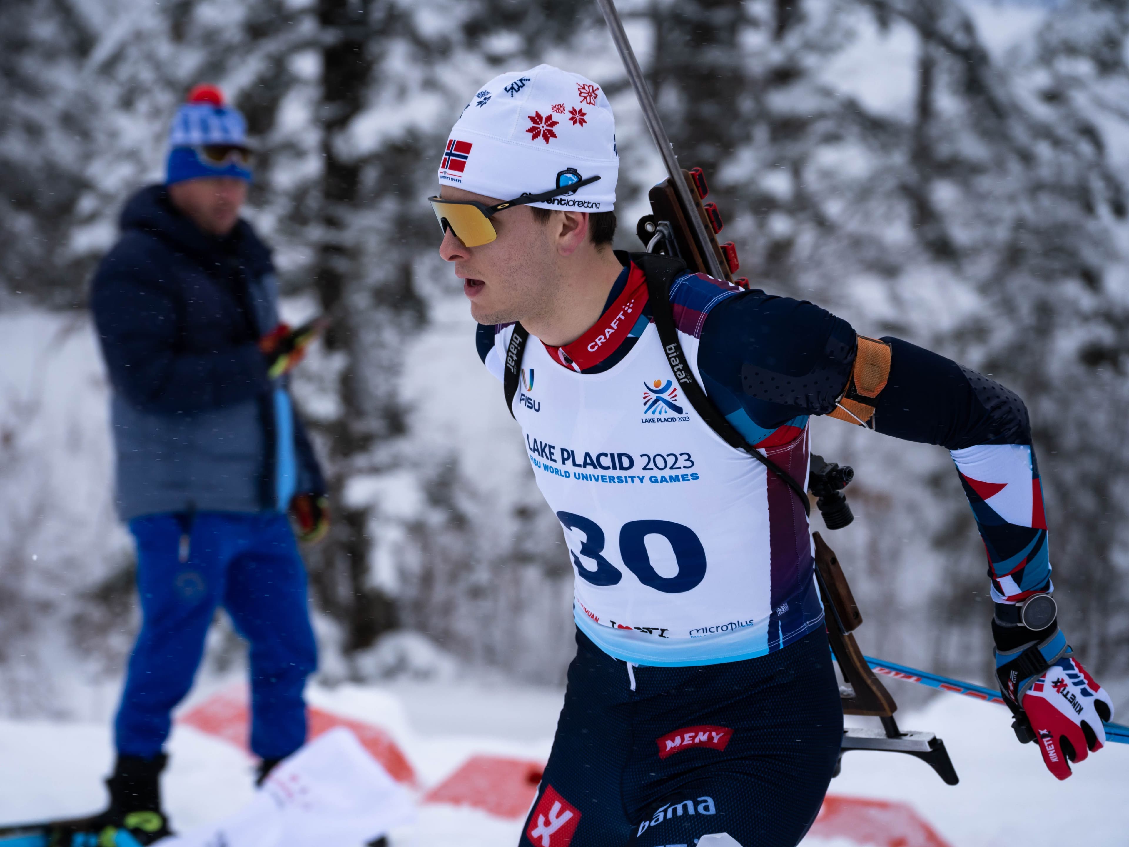 En skiskytter med startnummer 30 og gevær på ryggen i løypa i snøvær.
